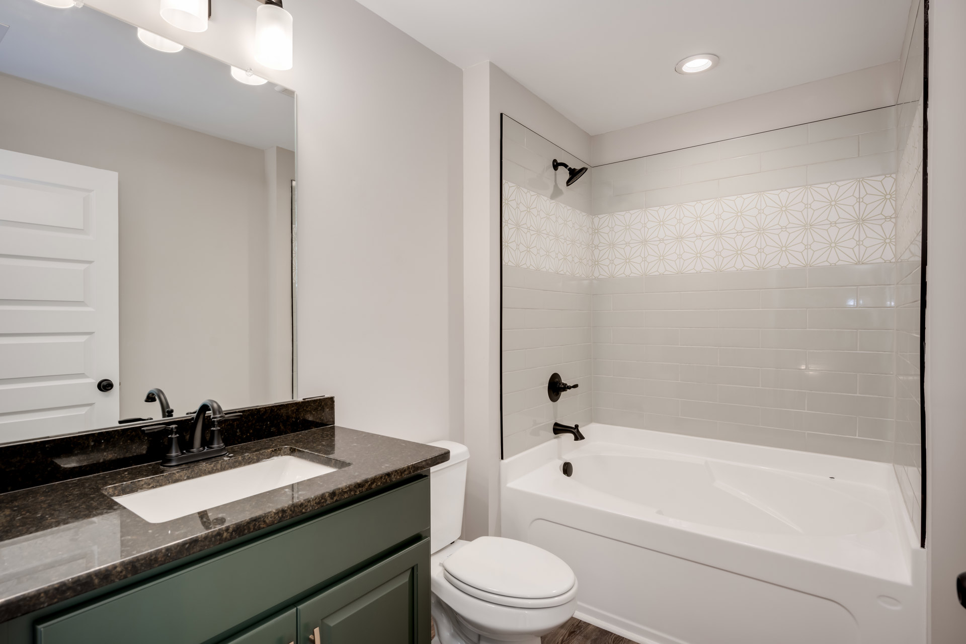 Bathroom with white bathtub set against a tiled wall, white toilet with closed lid, sink with countertop and mirror, and a close-up view of a door.