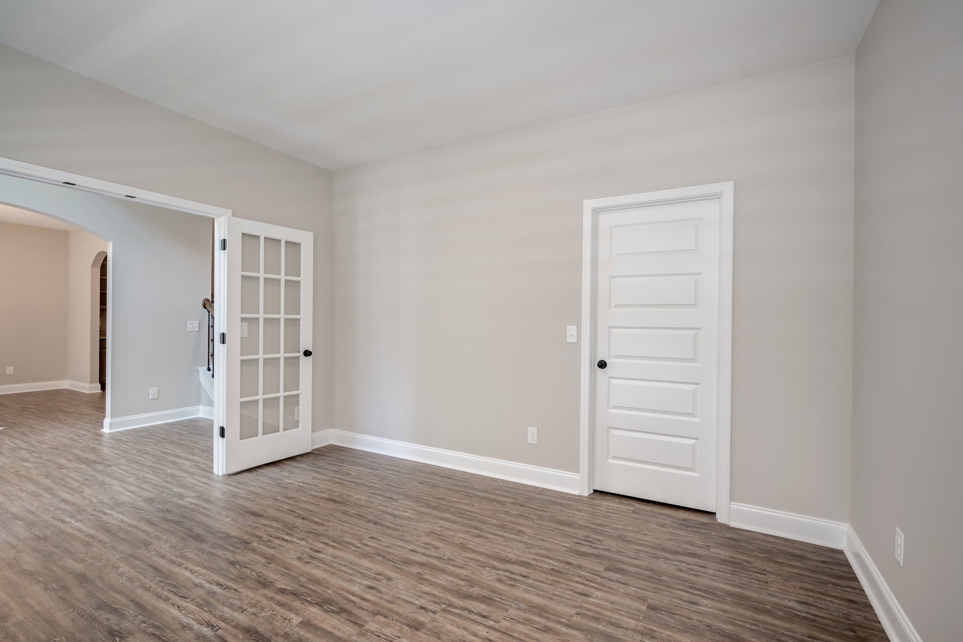 White walls, white door with black knob and glass panes, wood laminate flooring, wall-mounted power outlet, white corner surface