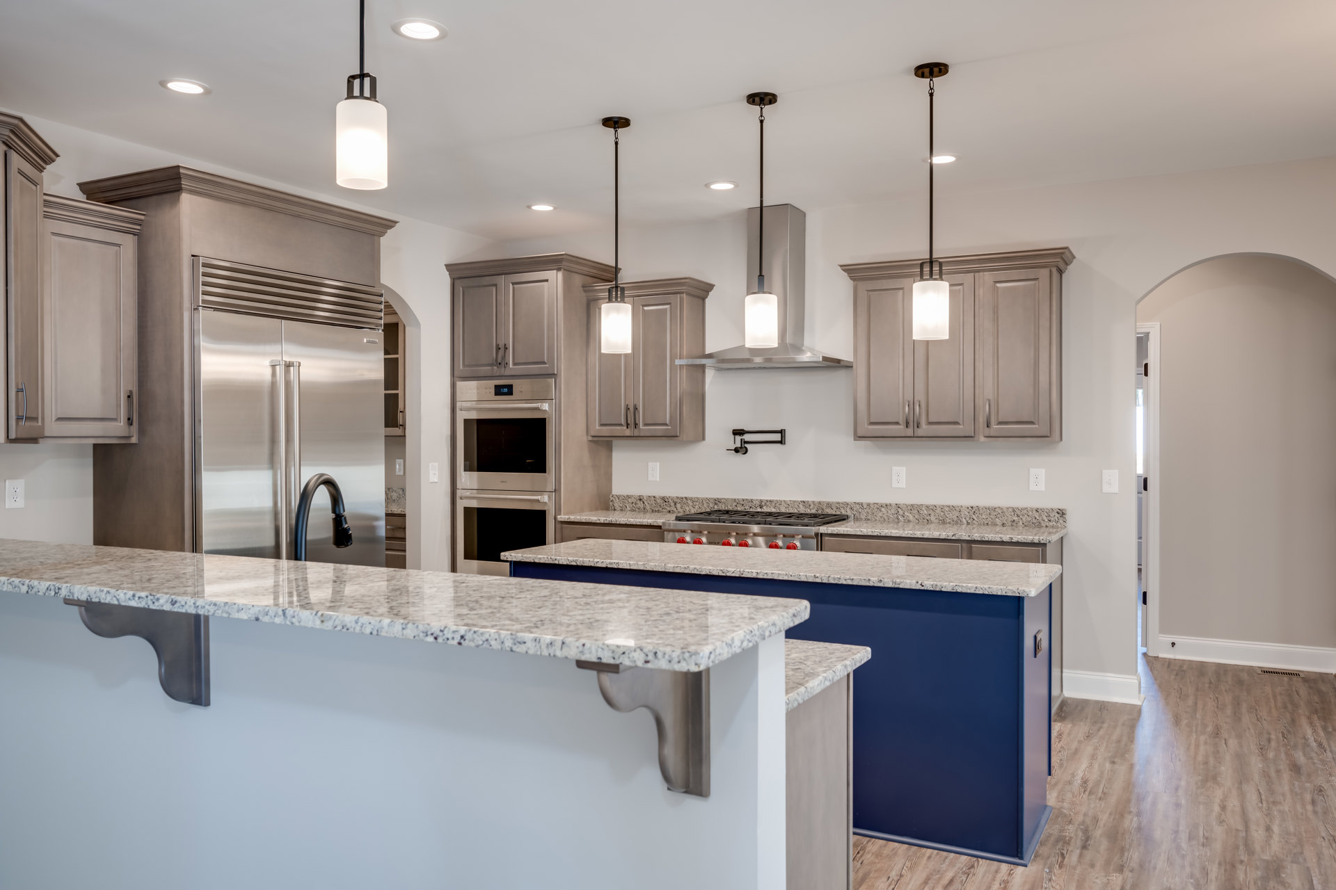 Granite countertops, stainless steel refrigerator, tile backsplash, white cabinetry, built-in oven with glass door, modern ceiling light fixture, chrome sink faucet