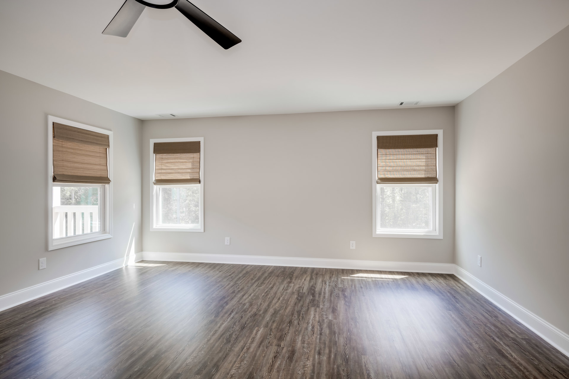 Wood flooring in a room with white plaster walls, ceiling fan, and window featuring a brown shade