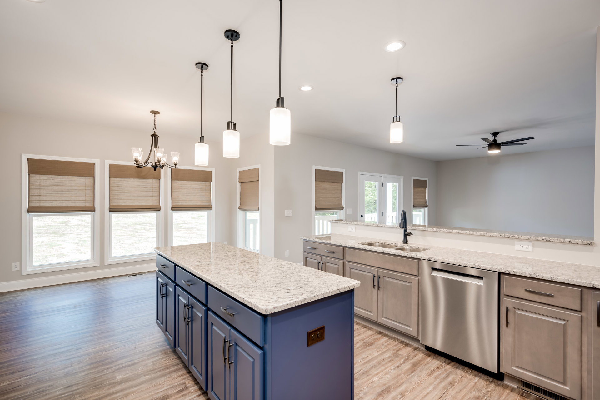 Kitchen with marble-topped island featuring built-in sink, silver dishwasher with black handle, white pendant light above, tile backsplash, brown window shade, and white cabinetry
