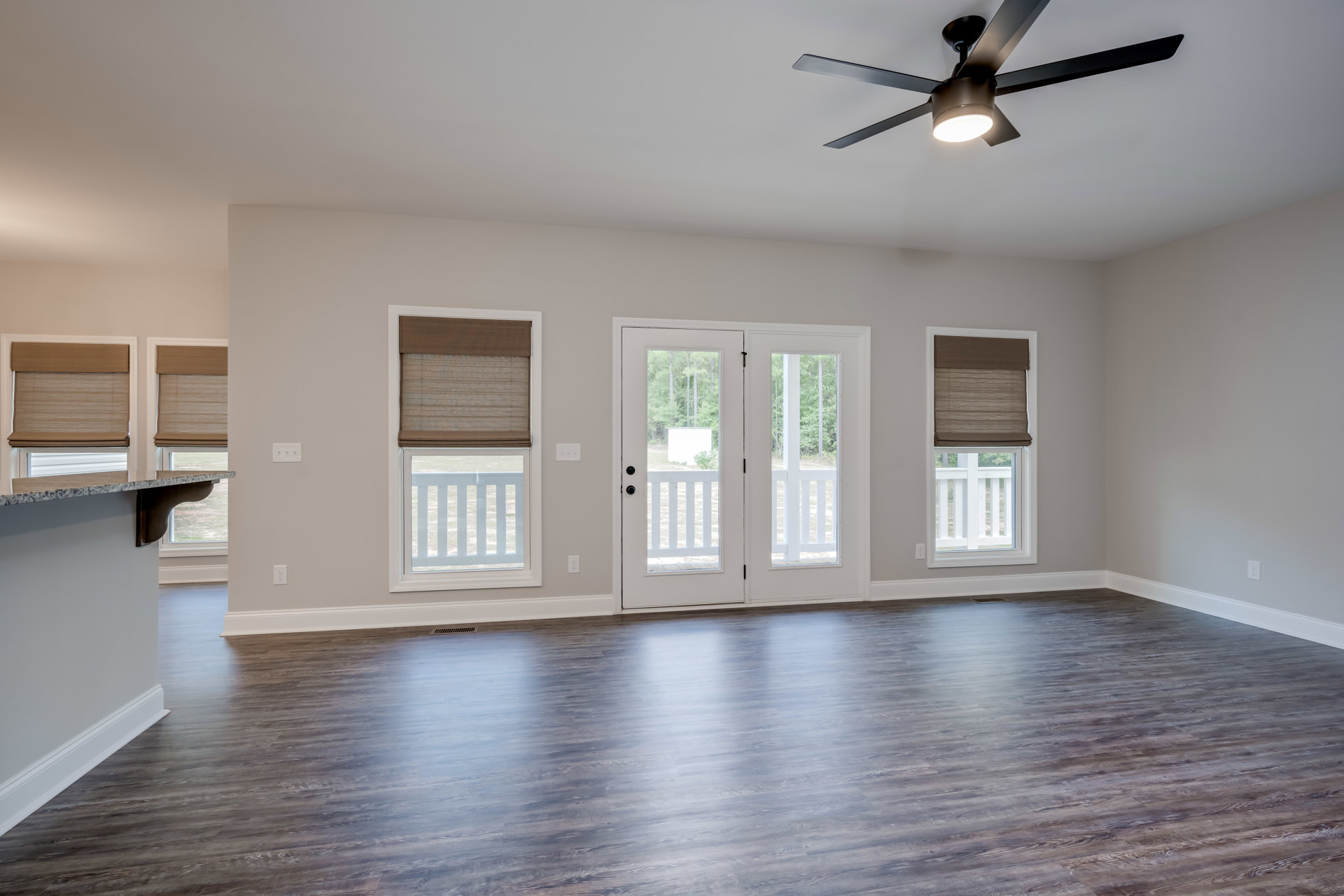 Ceiling fan with light fixture, hardwood flooring, white walls, large windows with brown shades, white double doors with glass panes