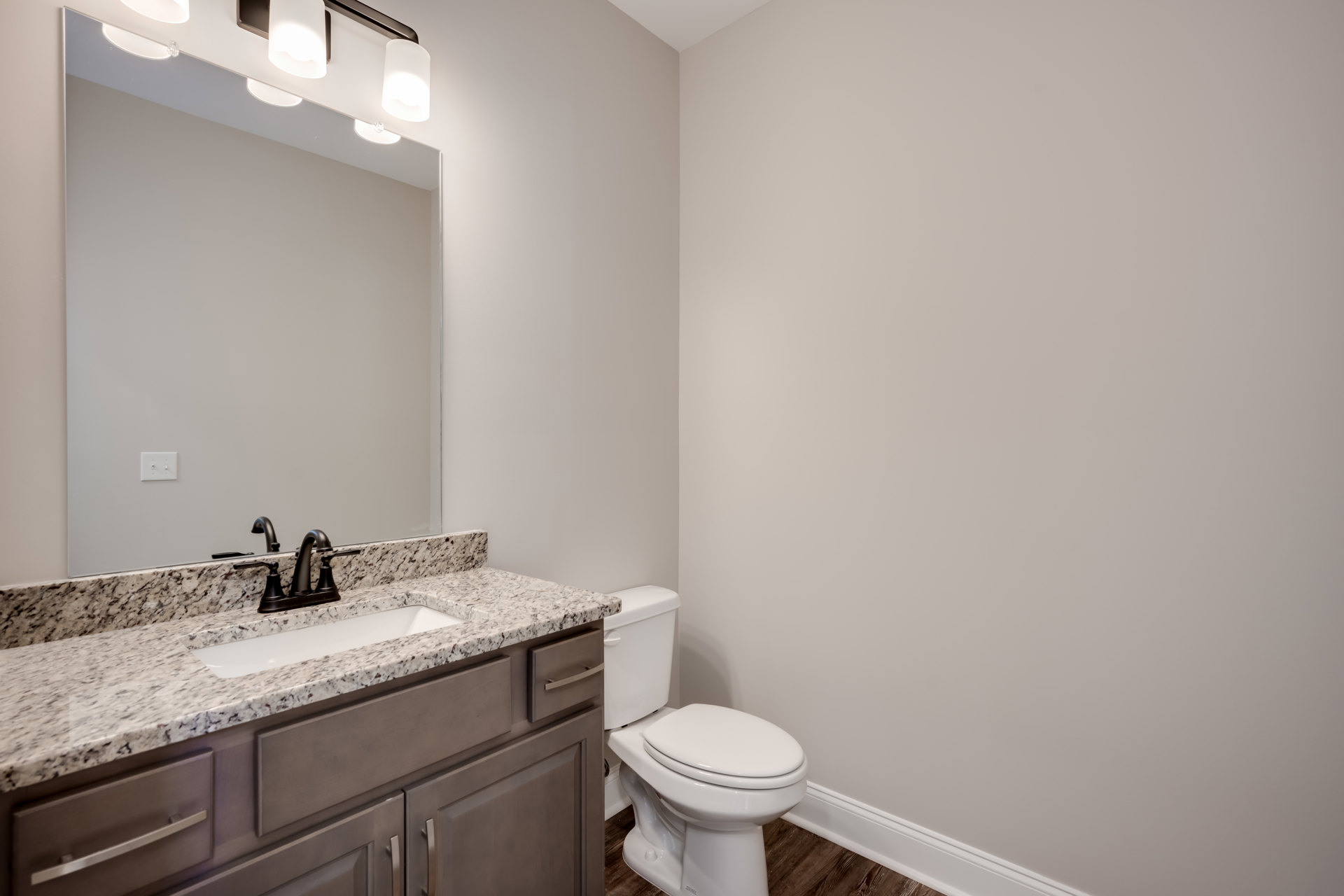 Marble countertop with undermount sink, chrome faucet, white toilet, light wood cabinetry, and neutral tile walls in a modern bathroom
