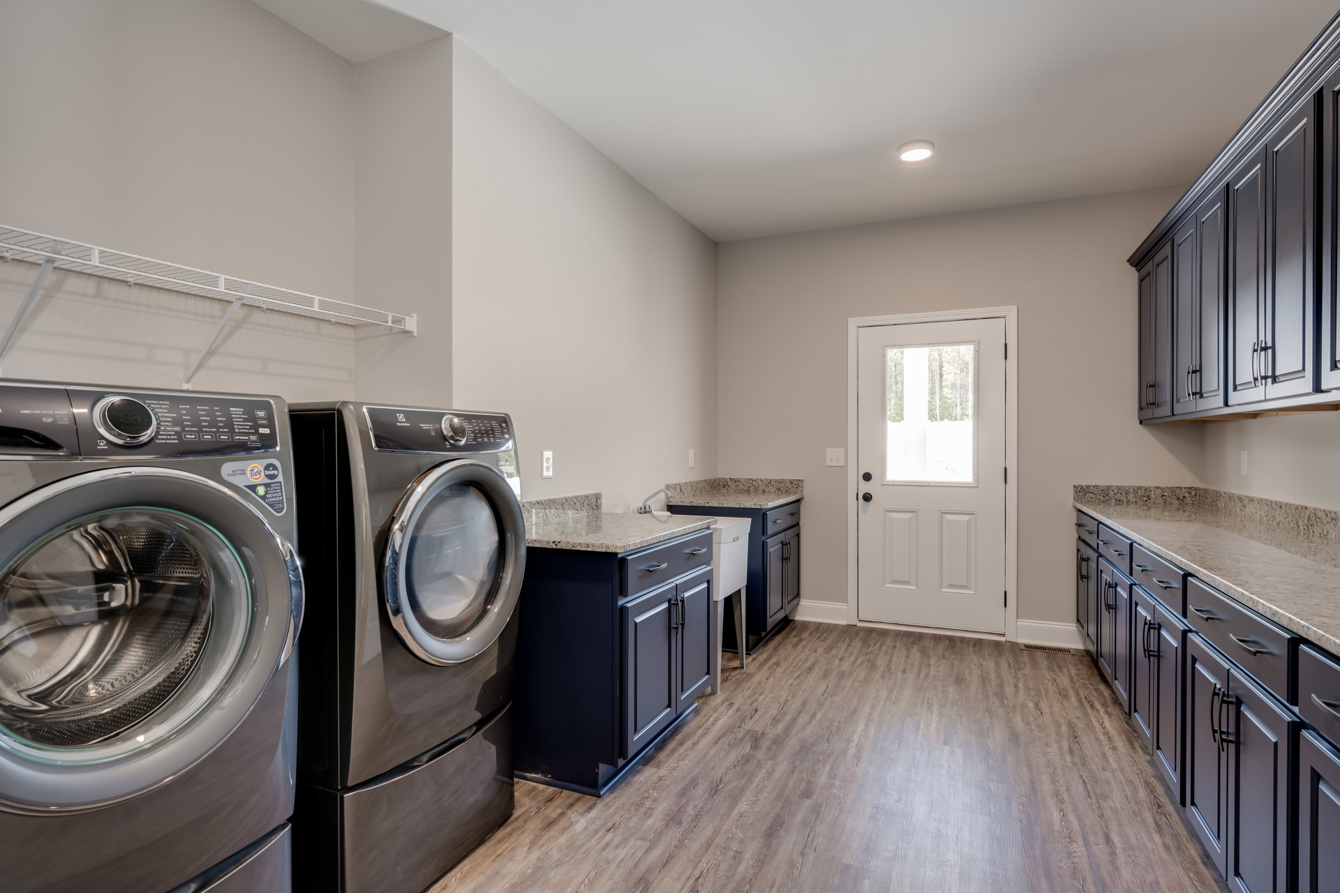 Laundry room with front-loading washer and dryer, white cabinetry, tile flooring, and a white door with glass window