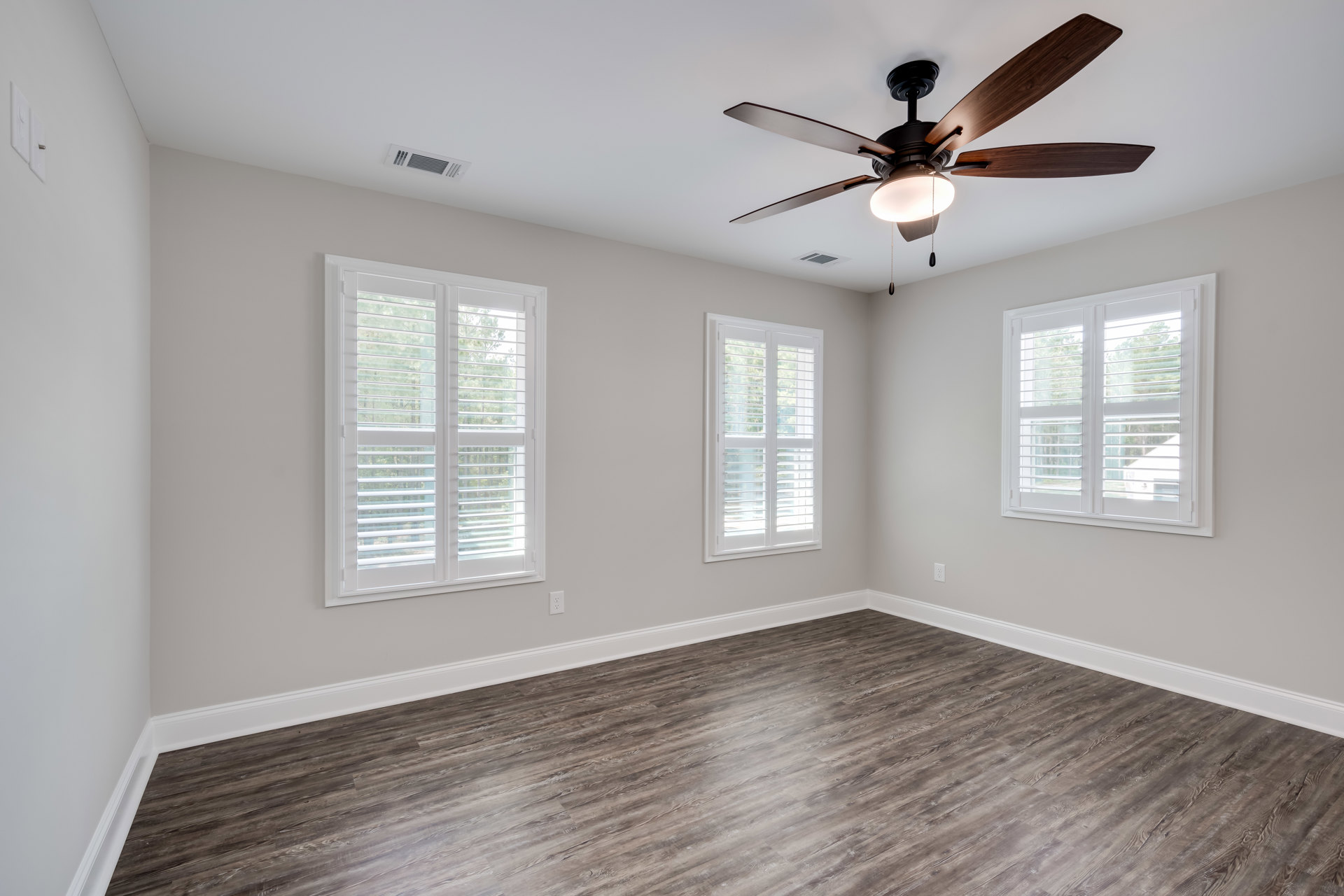 Ceiling fan with light fixture, two windows with white blinds, wood flooring with white baseboard trim, neutral walls, small black object on white windowsill