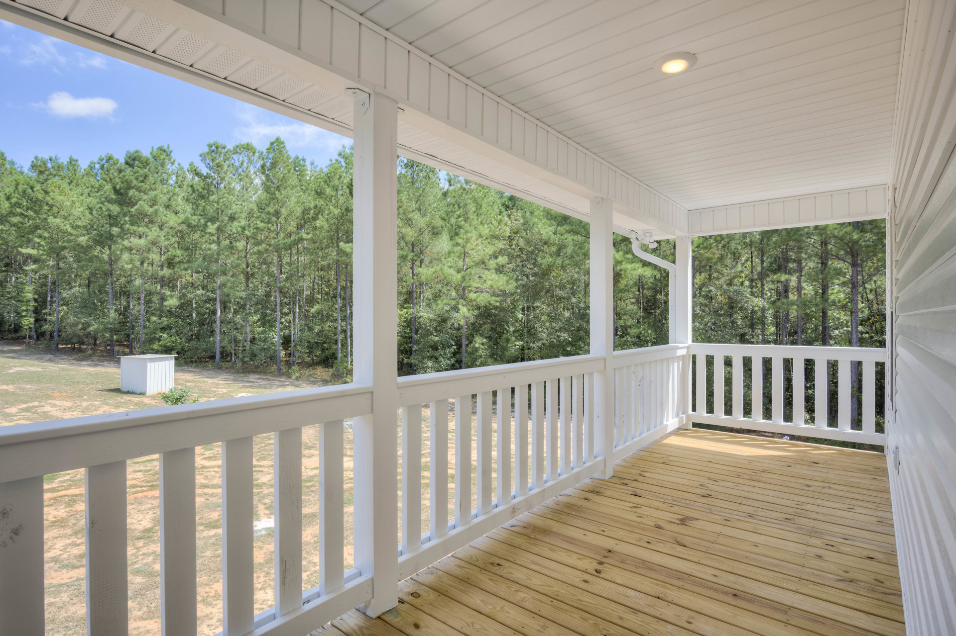 Wooden deck with white railing overlooking dense trees and a white shed in the background