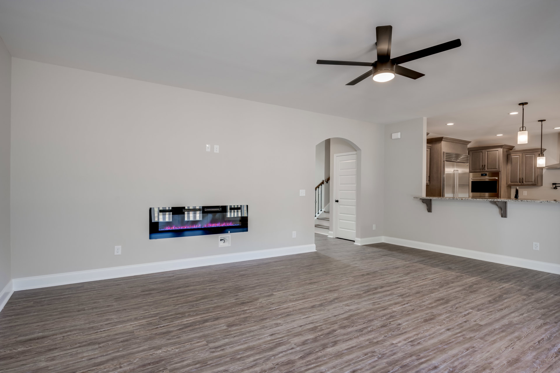 Living room with wood flooring, white walls, wall-mounted glass fireplace, ceiling fan with light, and television.