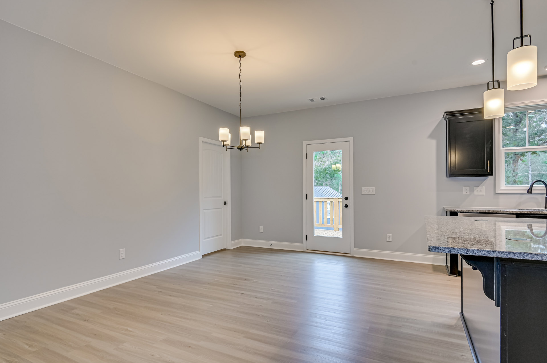 Living room with wood flooring, white walls, black cabinet topped with a white lamp, wall-mounted television, glass-paneled door, and ceiling light fixture with a white shade
