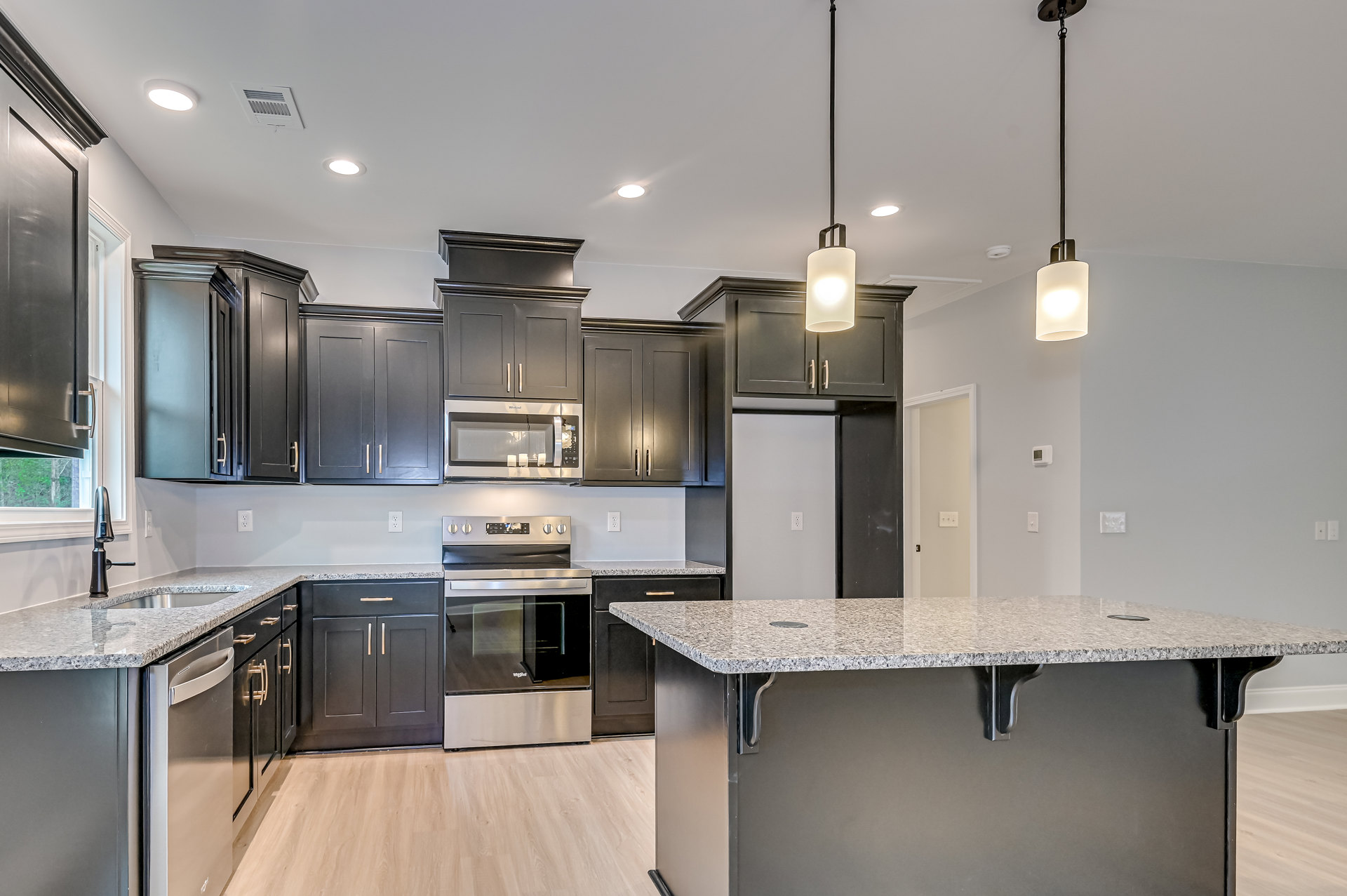 Granite island with undermount sink, stainless oven, white microwave, black floating shelf, curved pendant light, white cabinetry, and paneled door in a modern kitchen.