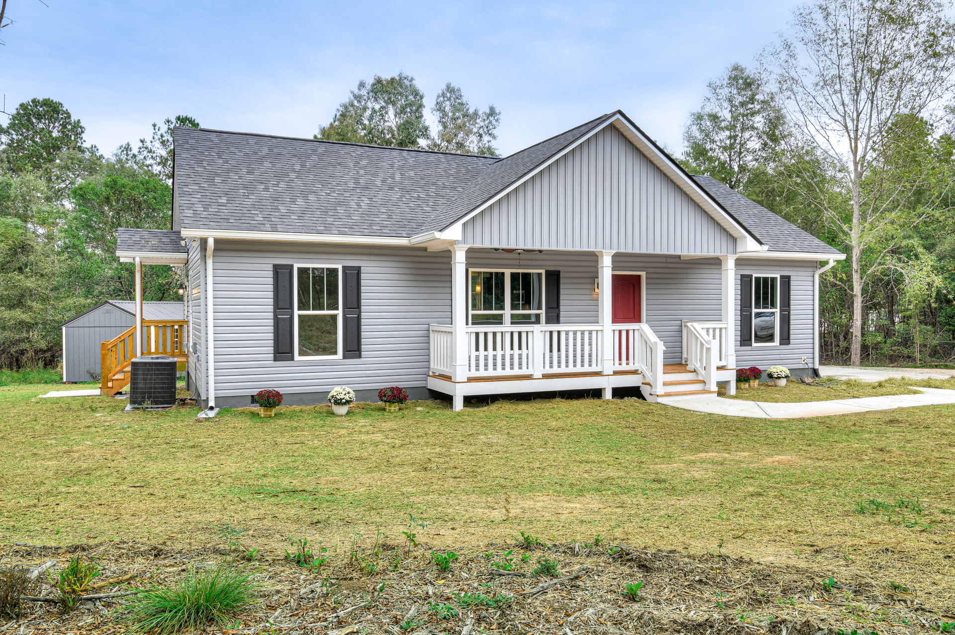 Red front door and white-framed windows on a cottage-style house with a porch, white railing, green lawn, and potted plant with white flowers.