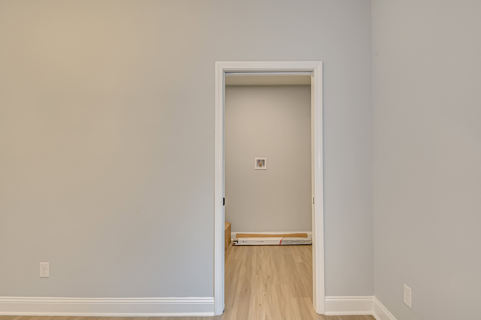 White paneled door set in a white plaster wall, wood flooring, small box mounted on wall and another box resting on floor