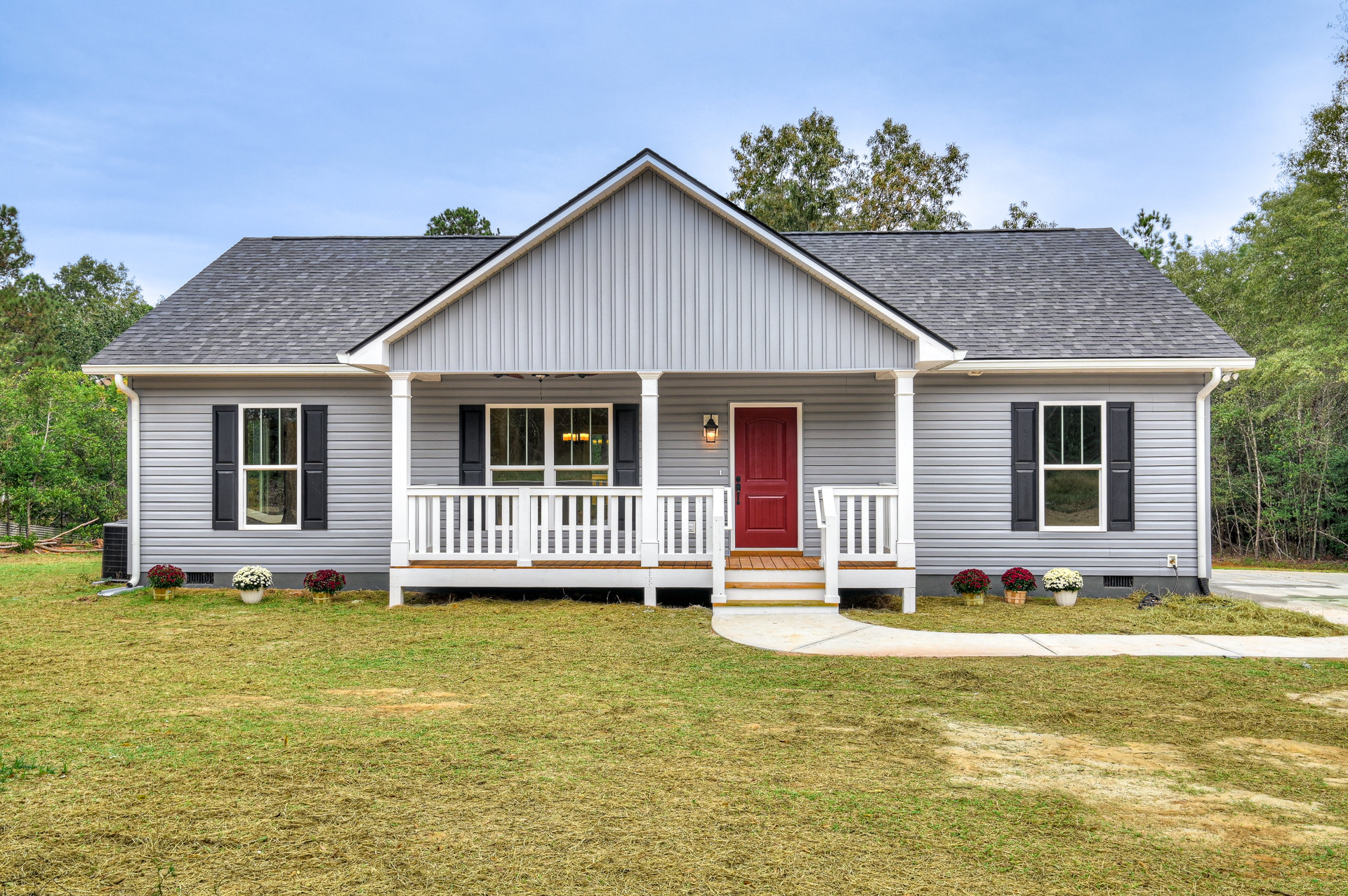 White siding house with two porches, red door with black handle, black shuttered window, white porch railings, basket of red flowers, green grass lawn