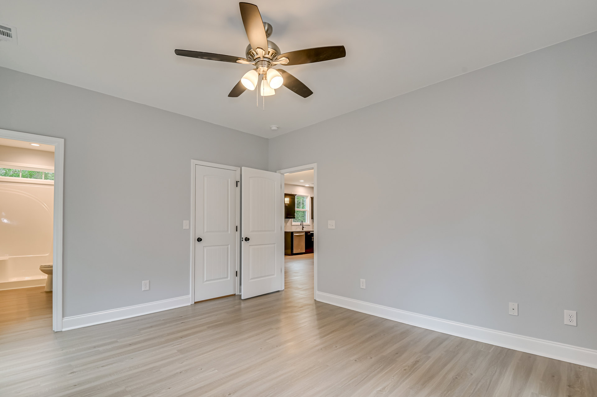 Ceiling fan with light fixture mounted on white ceiling, wood laminate flooring, white walls, white door with black knob