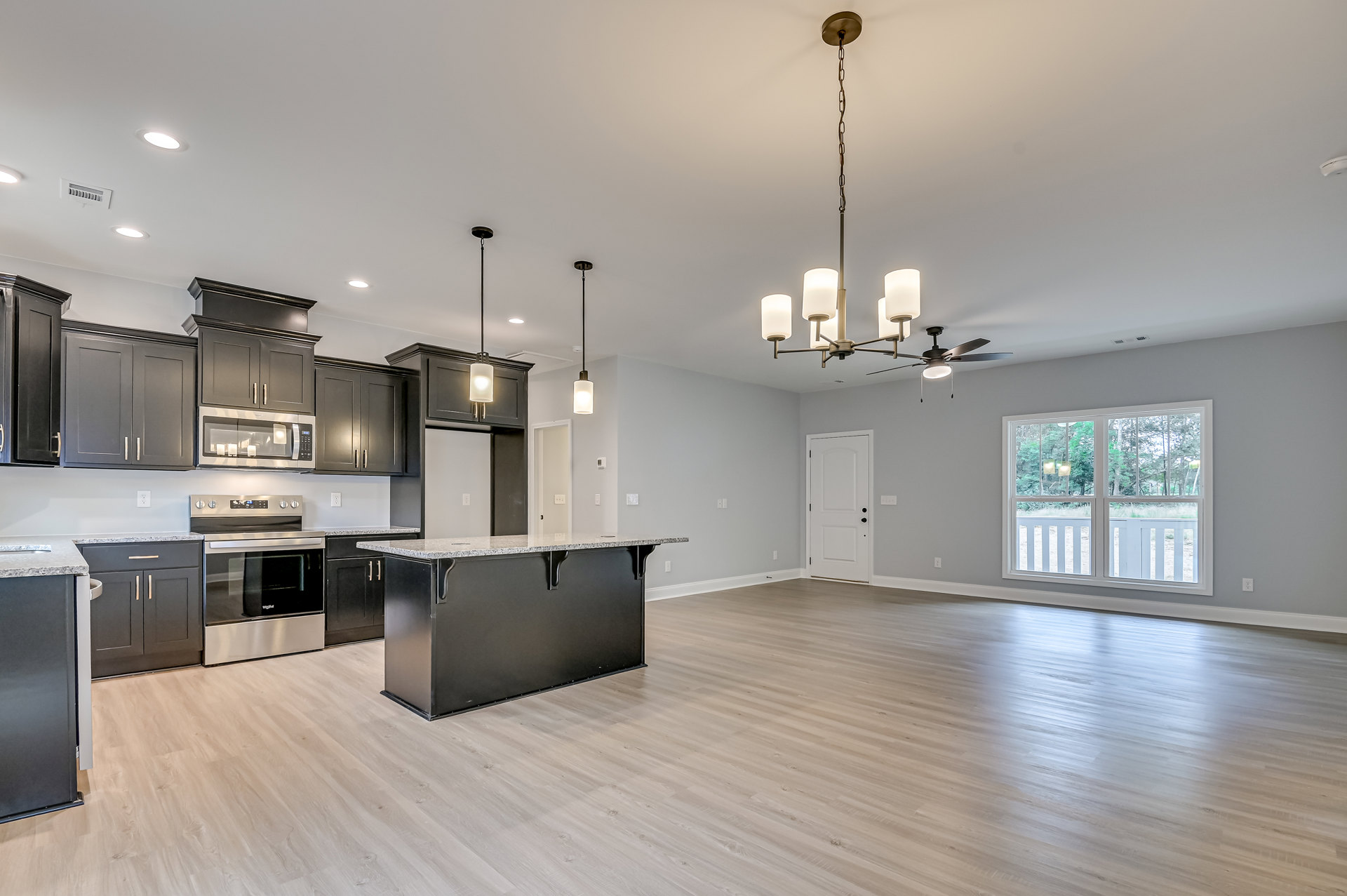 Open kitchen and dining area with wood flooring, black marble-topped counter, stainless steel stove and oven, grey wall, glass shelf holding candles, large window overlooking