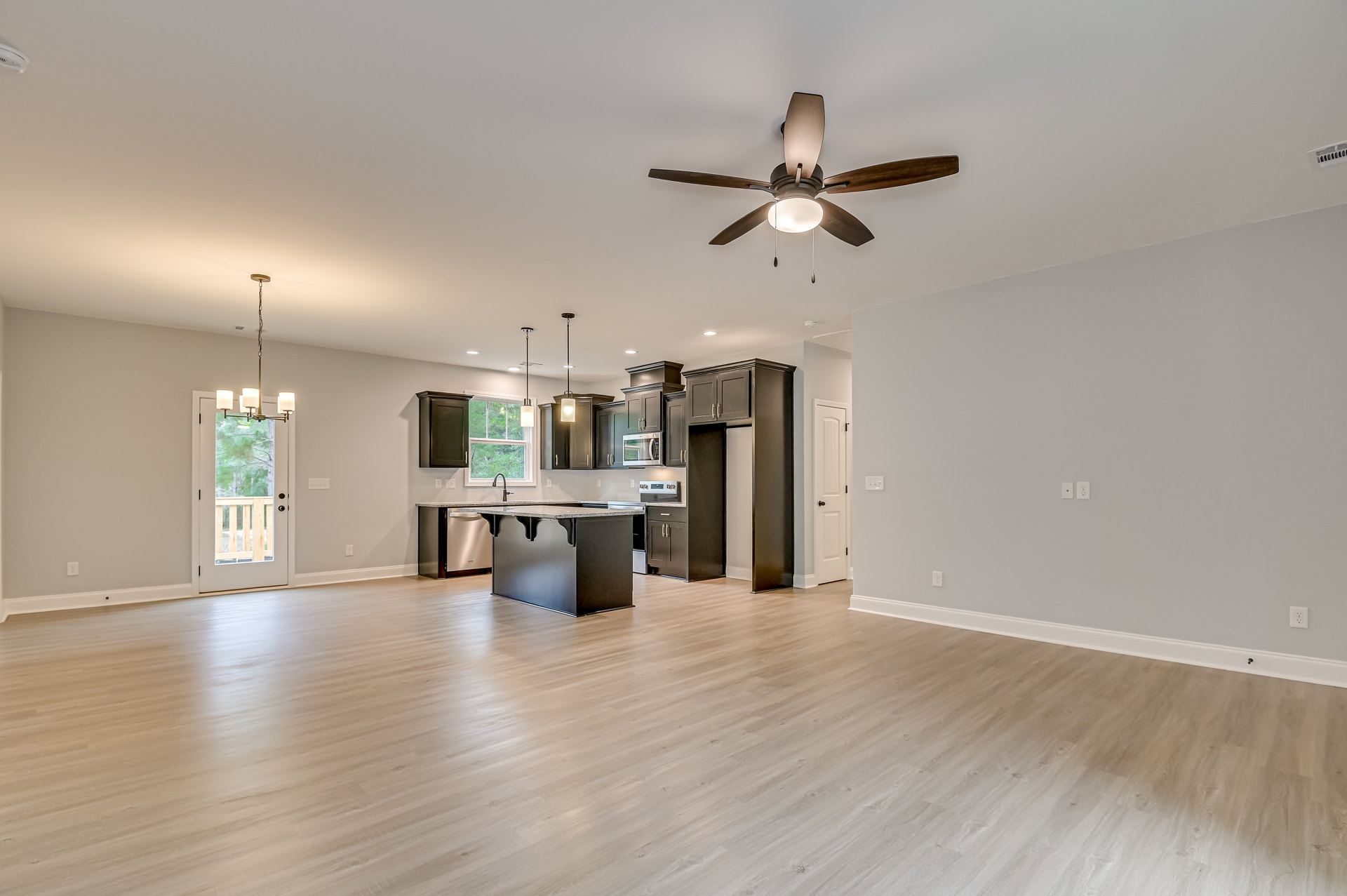 Open-concept kitchen and living room featuring a ceiling fan with light, black cabinets, marble countertop, wood flooring, and a glass-paneled door.