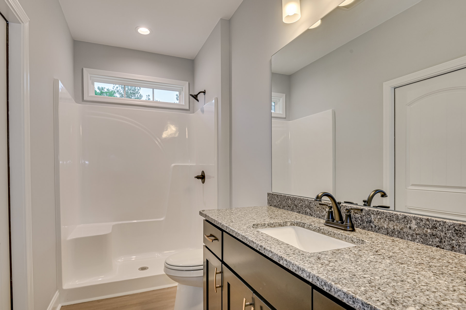 Modern bathroom featuring a white ceramic sink with chrome faucet, glass-enclosed shower, white toilet, tiled walls, and a window overlooking trees