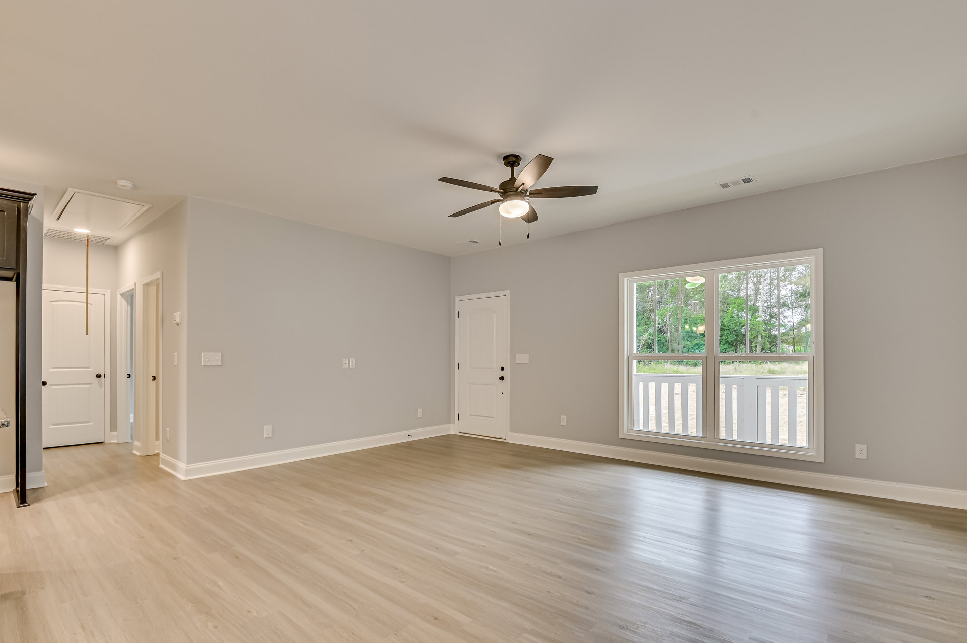 Ceiling fan with light fixture, wood laminate flooring, white plaster walls, window overlooking trees, white door with metal handle