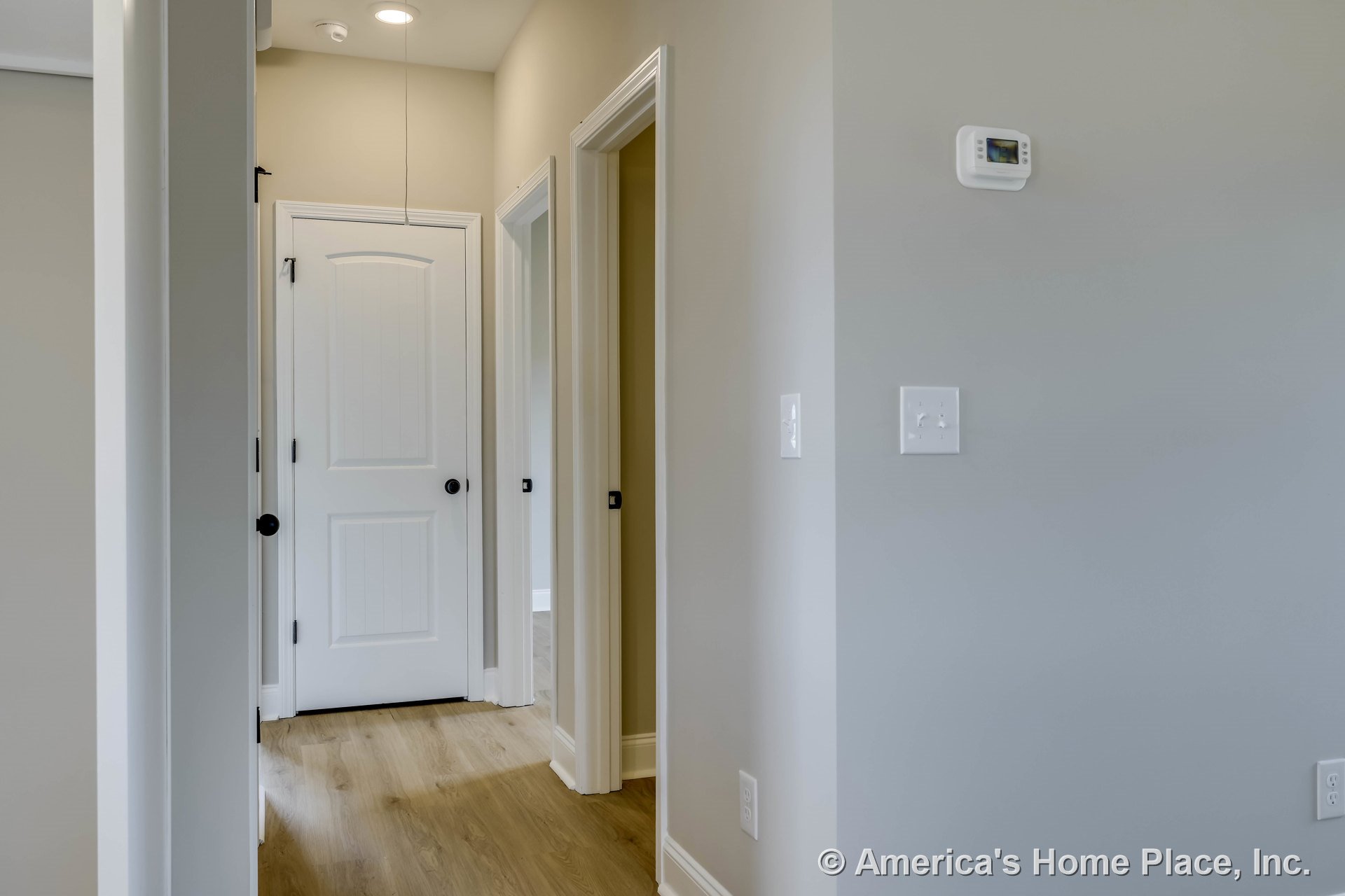 Hallway with light wood plank flooring, white paneled interior doors, neutral wall paint, baseboard trim, recessed ceiling lighting, wall-mounted thermostat, modern door hardware
