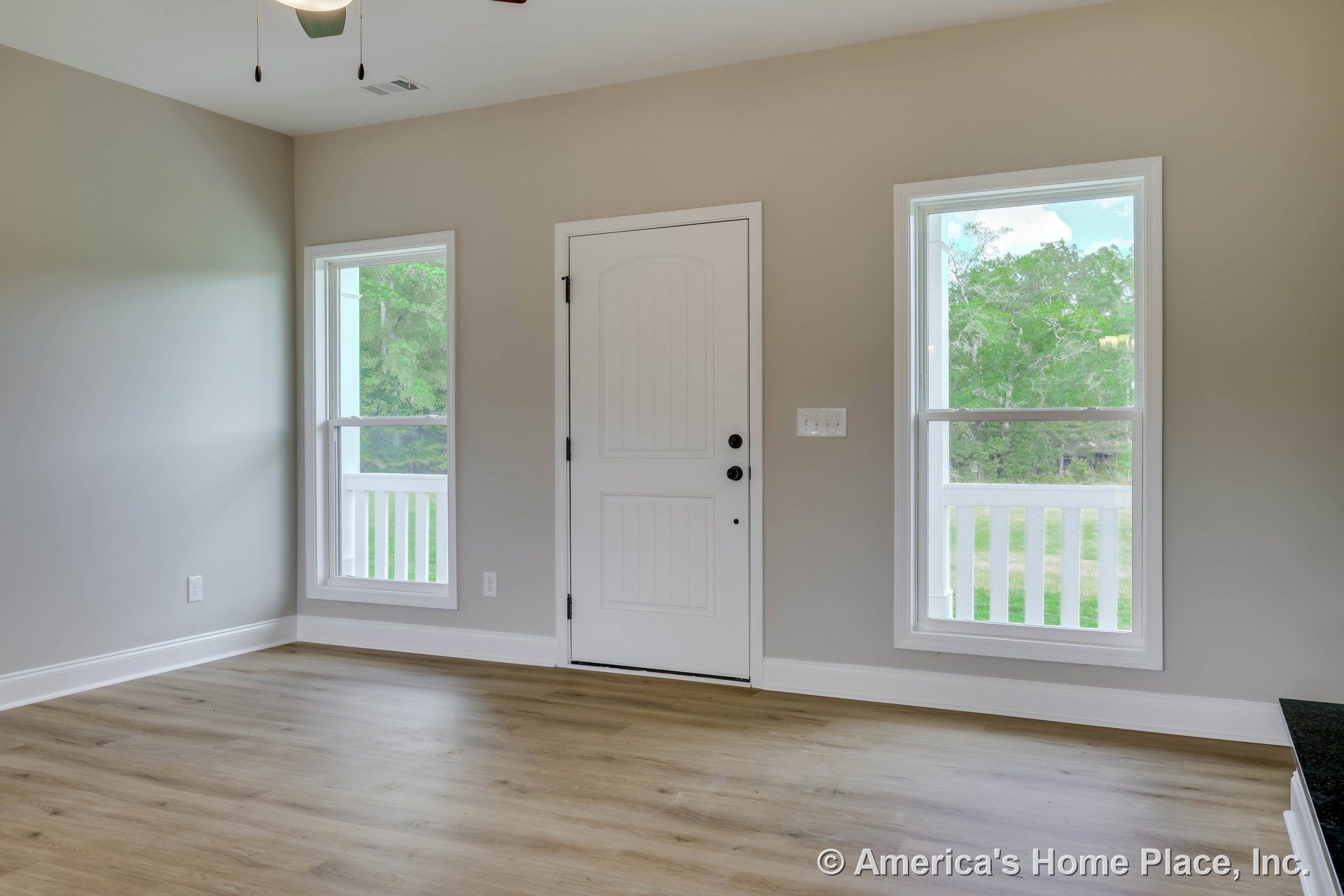White paneled front door with modern door hardware, two tall windows allowing natural light, light wood plank flooring, neutral wall paint, white baseboards and trim, ceiling light