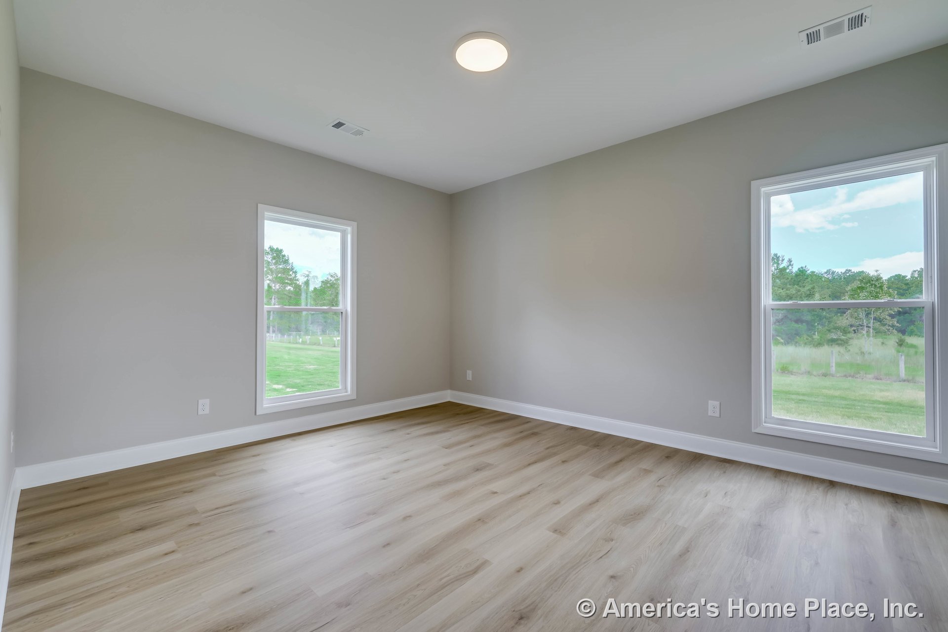 Bedroom with light vinyl plank flooring, two large windows framed in white trim, neutral wall color, white baseboards, and a flush ceiling light fixture.