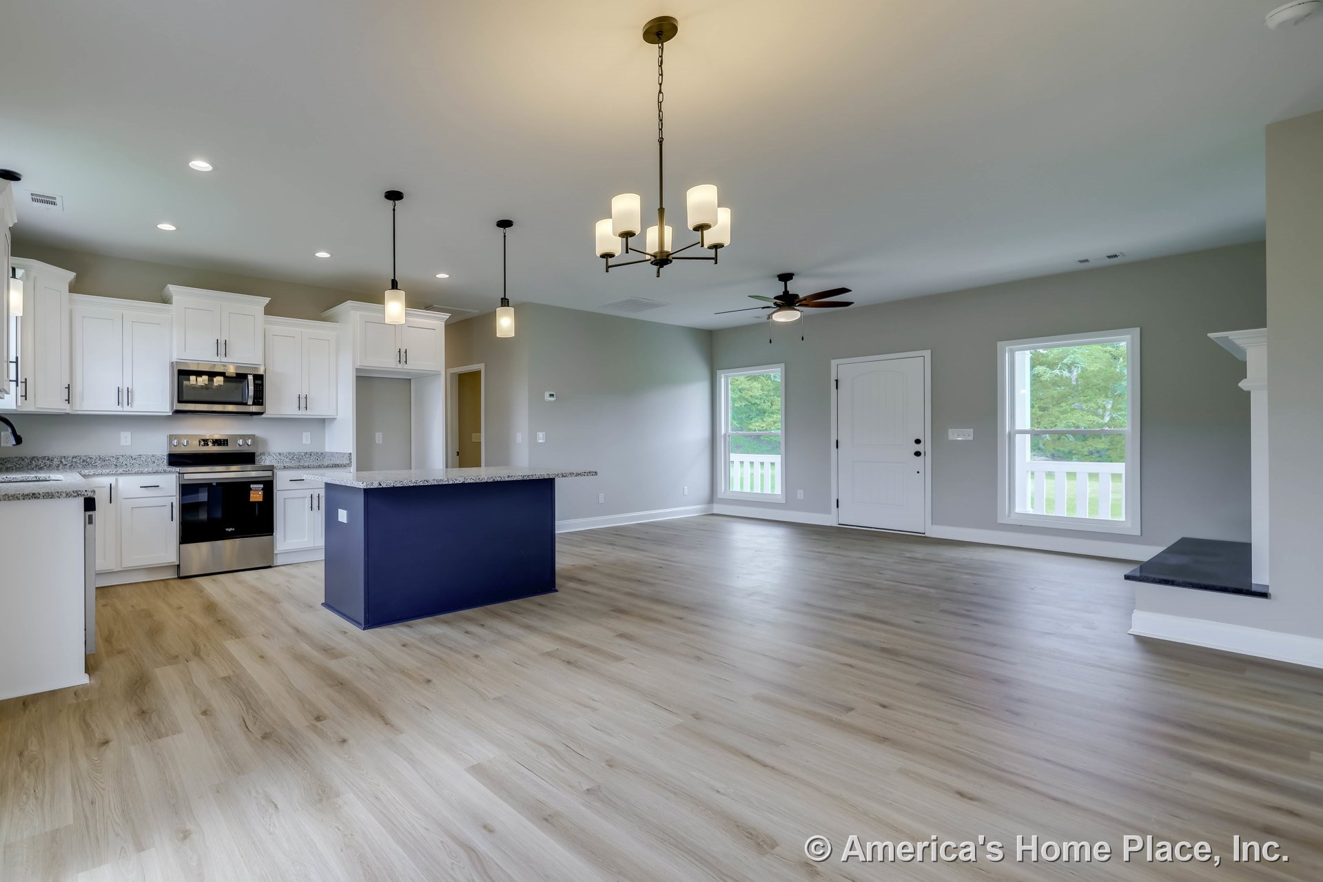 Open-concept kitchen and living area with white shaker cabinets, granite kitchen island, stainless steel appliances, pendant and chandelier lighting, light wood flooring, large