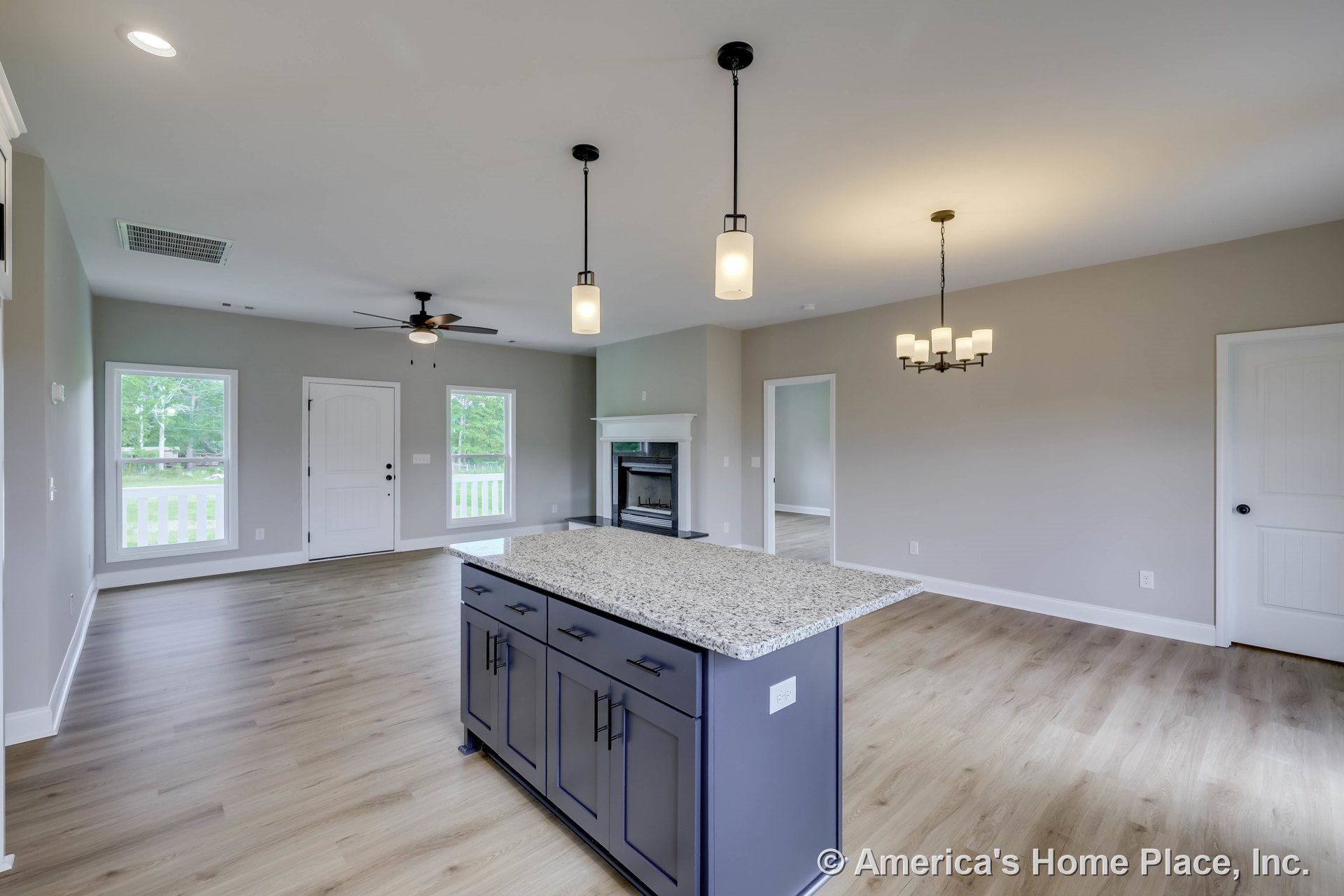 Open-concept living area with granite kitchen island, light wood plank flooring, built-in fireplace with mantel, pendant and chandelier lighting, white trim and interior doors, and