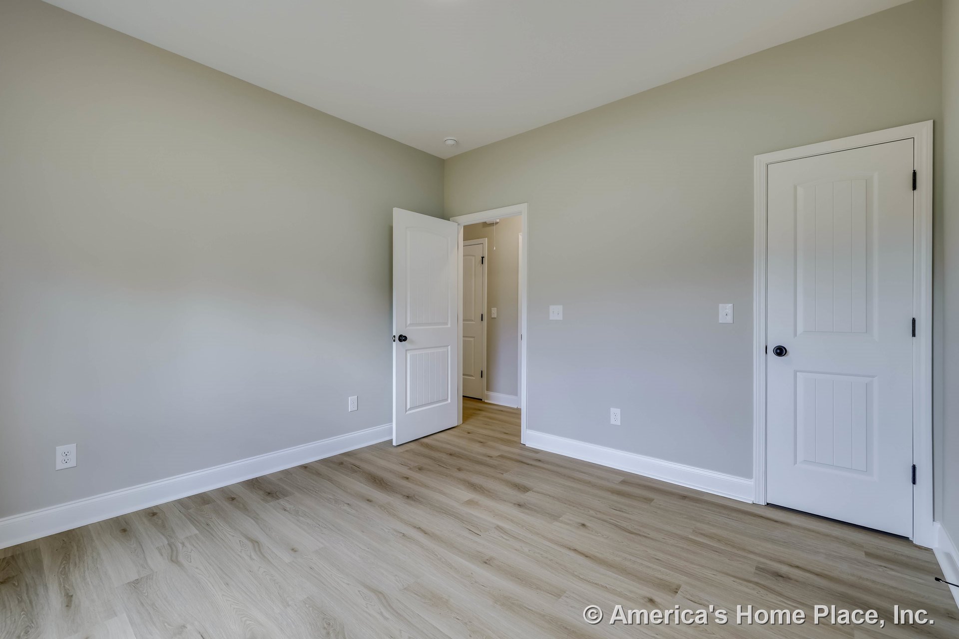 Bedroom with light wood-look vinyl plank flooring, gray painted walls, white baseboards, two paneled white doors with black hardware, and a smooth white ceiling.