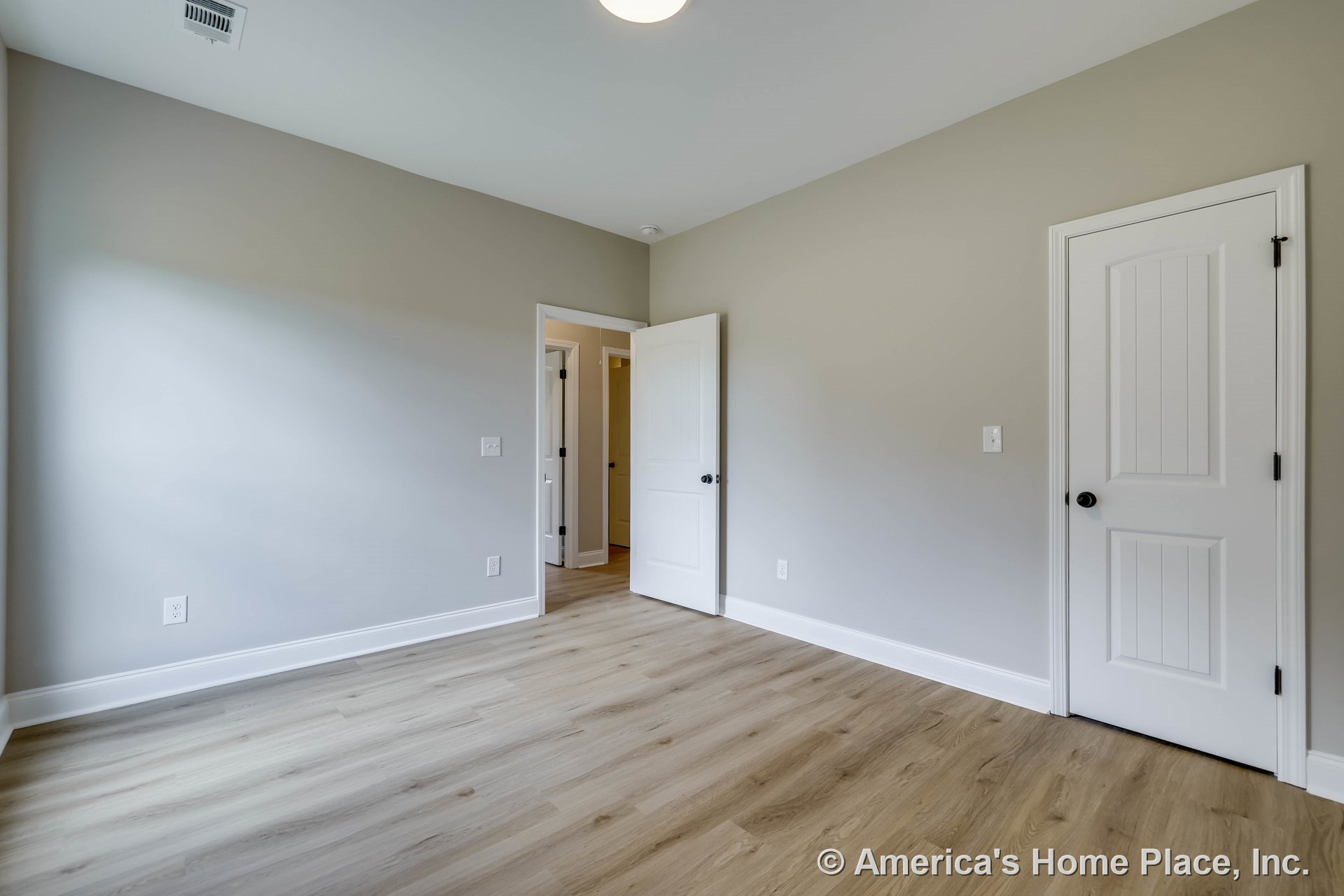 Bedroom with light wood-look laminate flooring, neutral painted walls, wide white baseboards, flush ceiling light, white paneled doors including closet door, and ceiling vent.