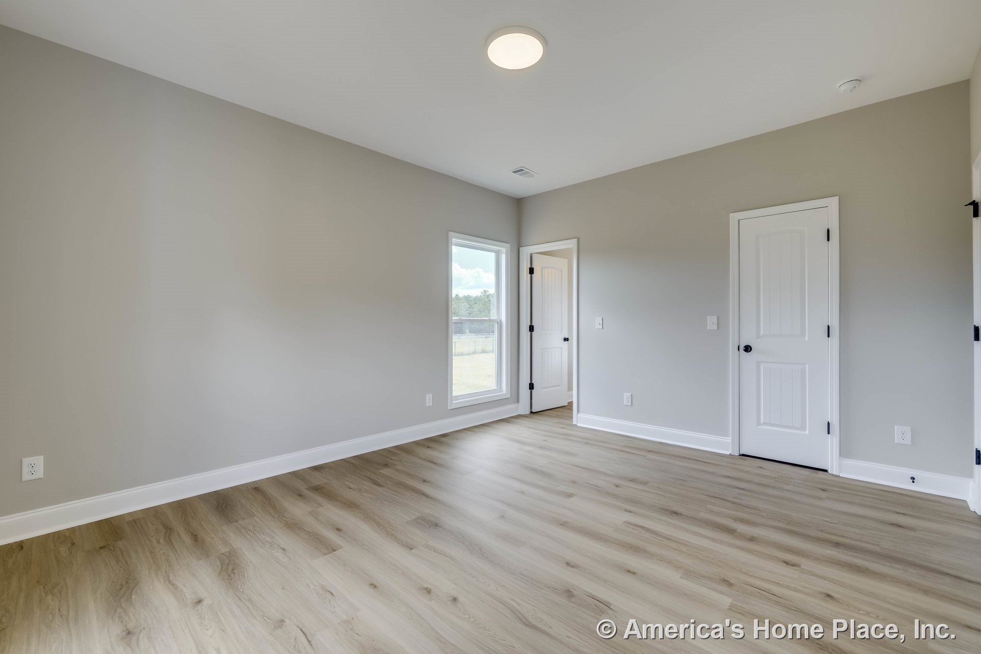 Bedroom with light wood laminate flooring, gray painted walls, wide white baseboards, single window with white casing, flush mount ceiling light, and two paneled white doors with