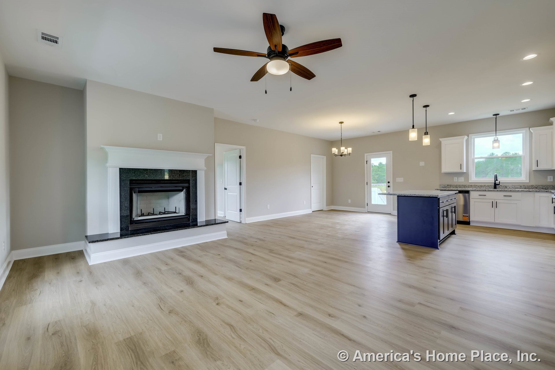 Open concept living area with black granite fireplace surround, light wood plank flooring, white shaker kitchen cabinets, granite countertops, ceiling fan with light, pendant and