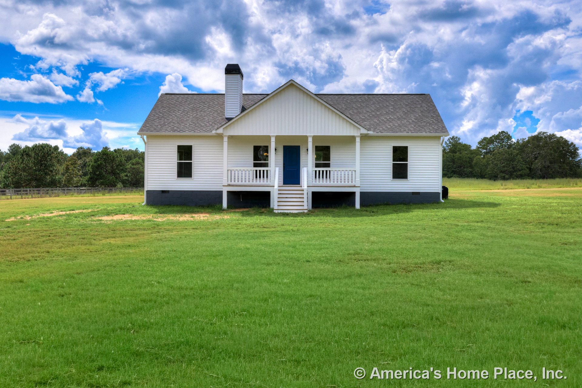 Covered front porch with white railings and steps, blue entry door, white horizontal siding, black foundation trim, symmetrical windows, left-side chimney, gabled roof, rural
