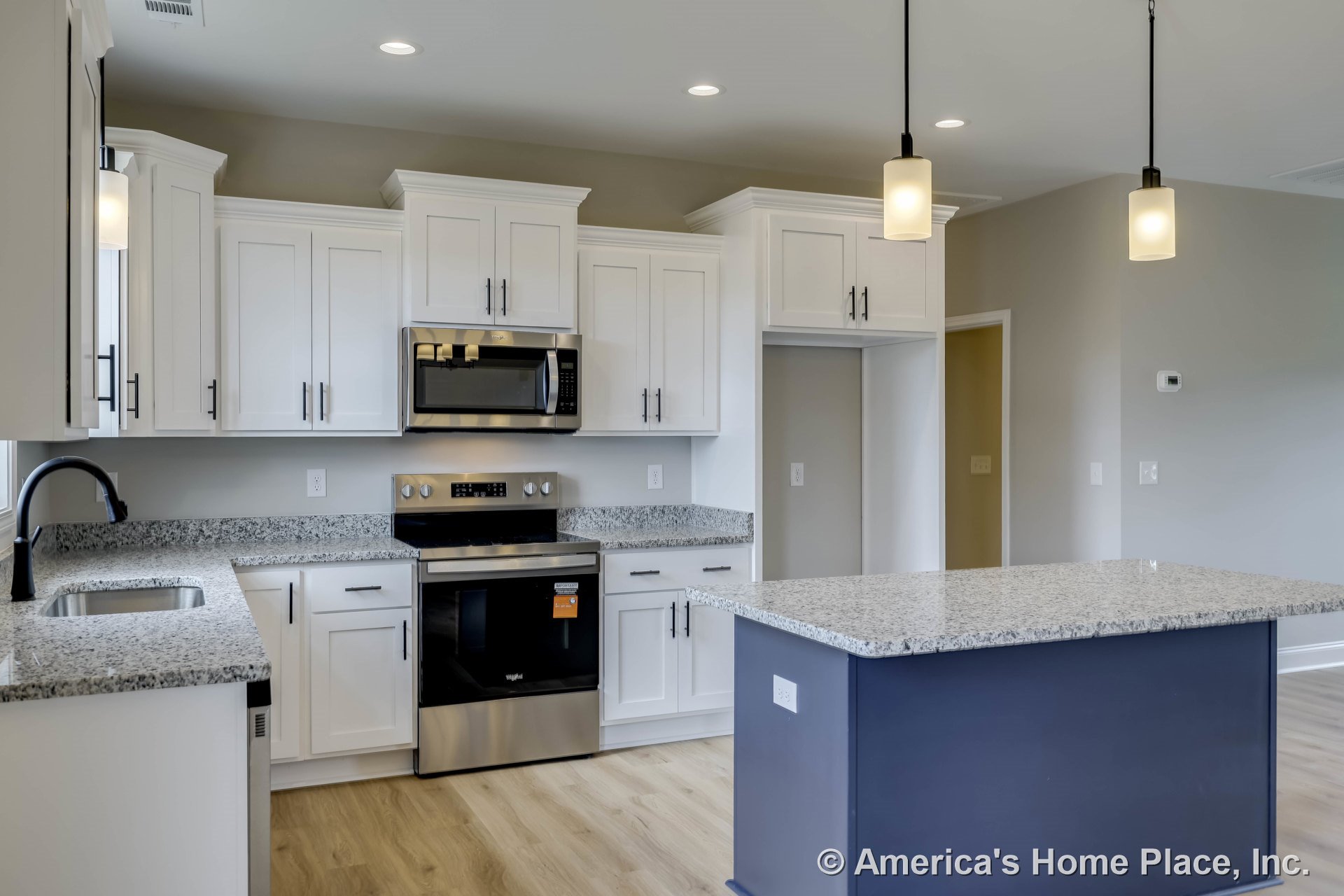 White shaker cabinets and granite island countertop with built-in sink and black faucet, stainless steel oven and microwave, pendant and recessed ceiling lights, light wood