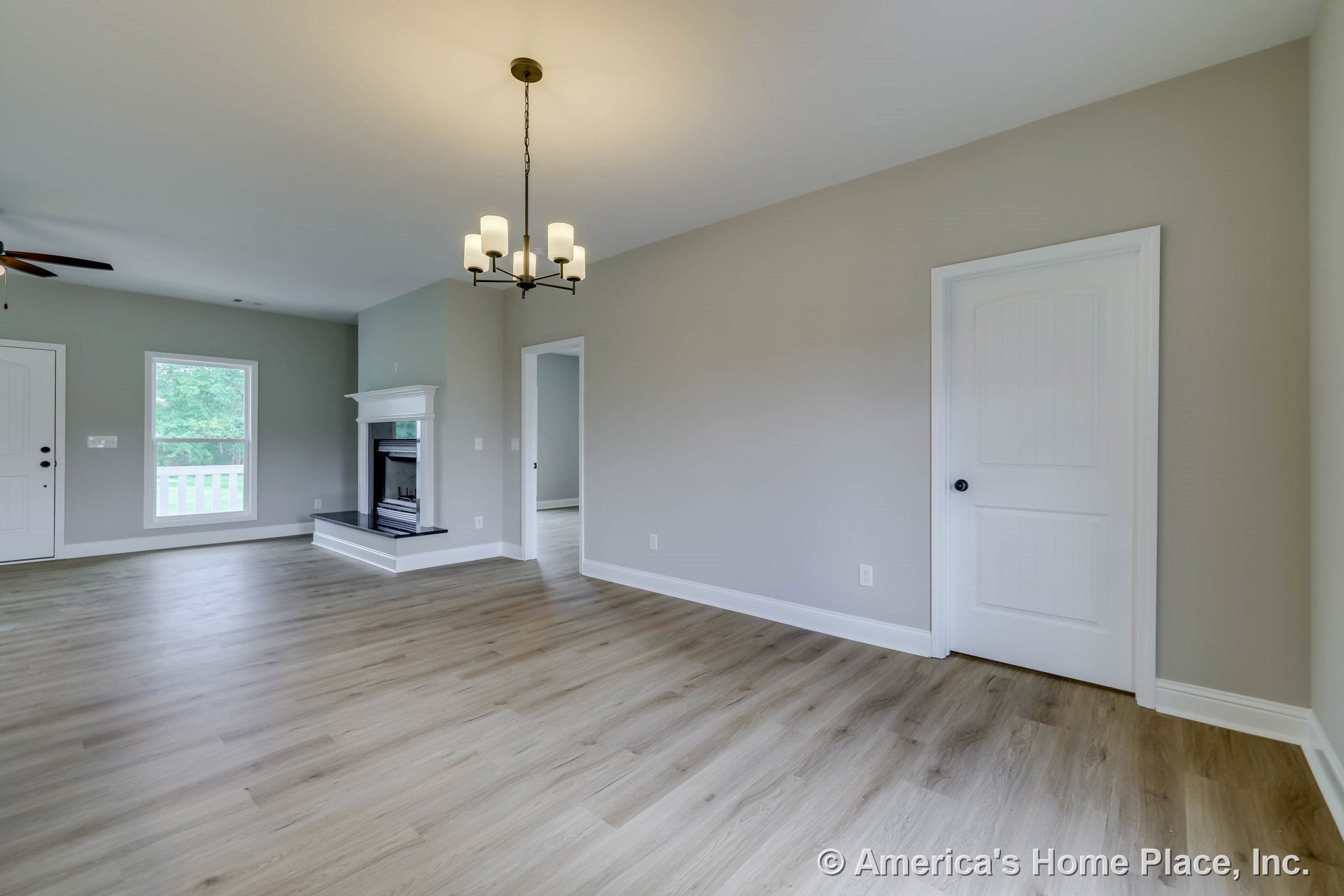 Light wood plank flooring, white fireplace with mantel and trim, modern ceiling chandelier, large window with white trim, neutral wall paint, paneled interior door, baseboards, and