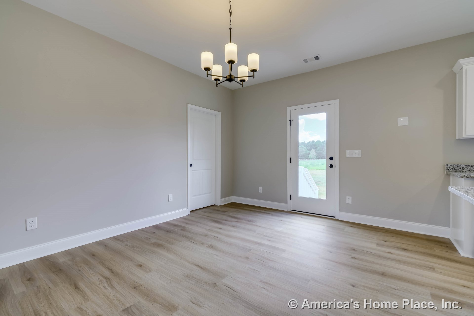 Dining area with light wood plank flooring, glass exterior door framed in white trim, modern chandelier featuring cylindrical shades, white baseboards, neutral wall color, and