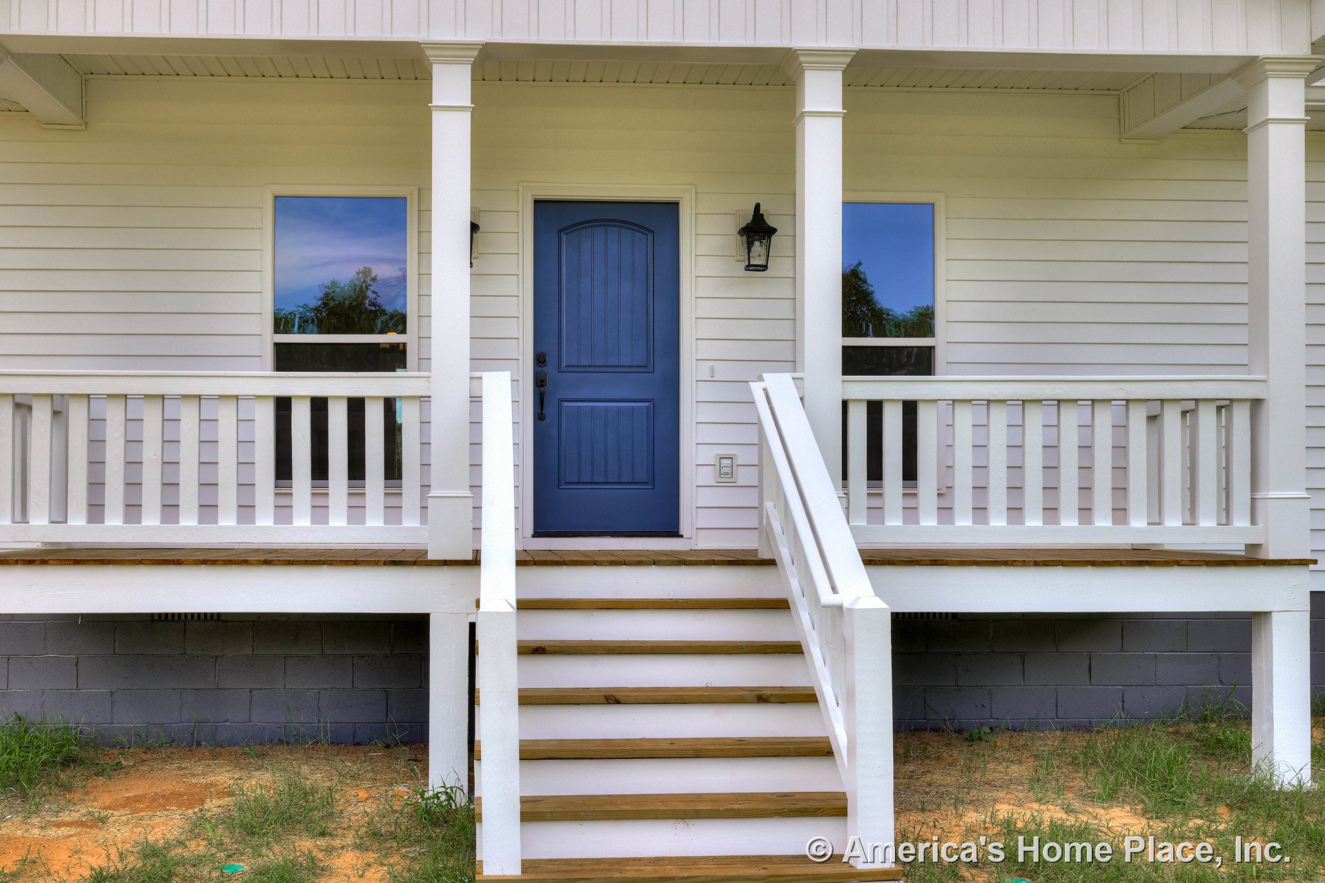 Covered front porch with white horizontal siding, blue paneled entry door, white railings, wooden steps, exterior wall lantern, porch ceiling, and decorative columns.