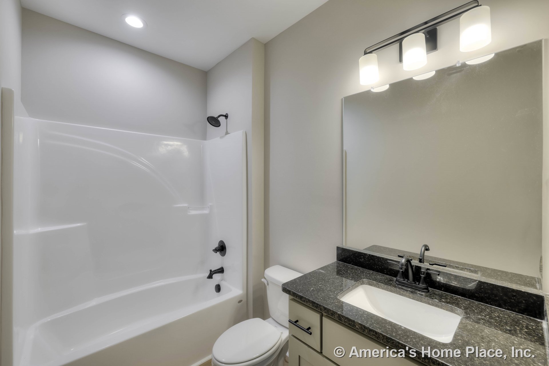 Built-in white acrylic tub and shower with black fixtures, granite vanity countertop, large wall mirror, three-light overhead vanity fixture, light-colored cabinetry, and neutral