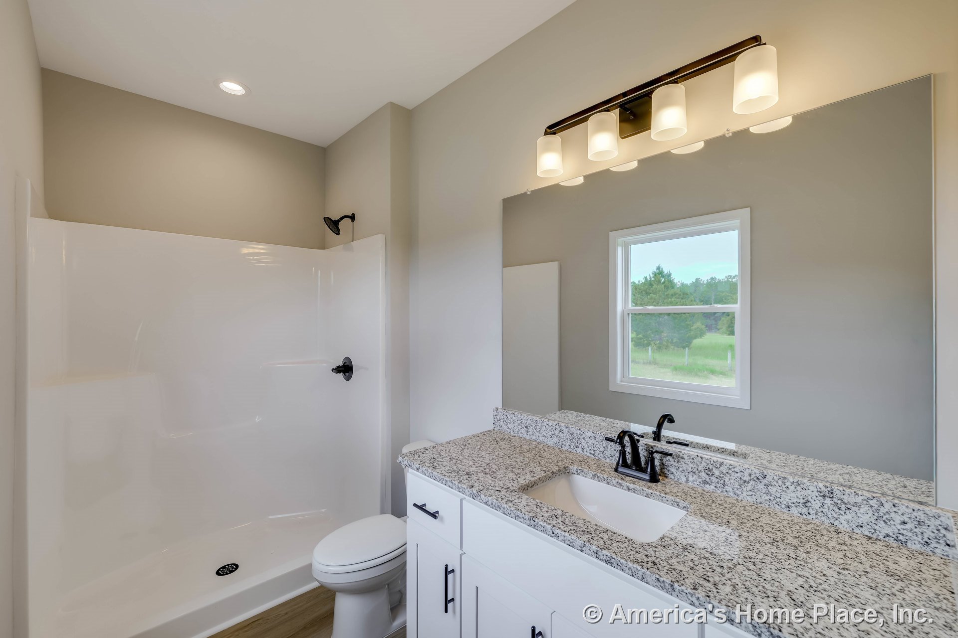 White fiberglass shower enclosure, granite vanity countertop with single sink, white shaker cabinetry, black faucet fixtures, large wall mirror, window with decorative trim