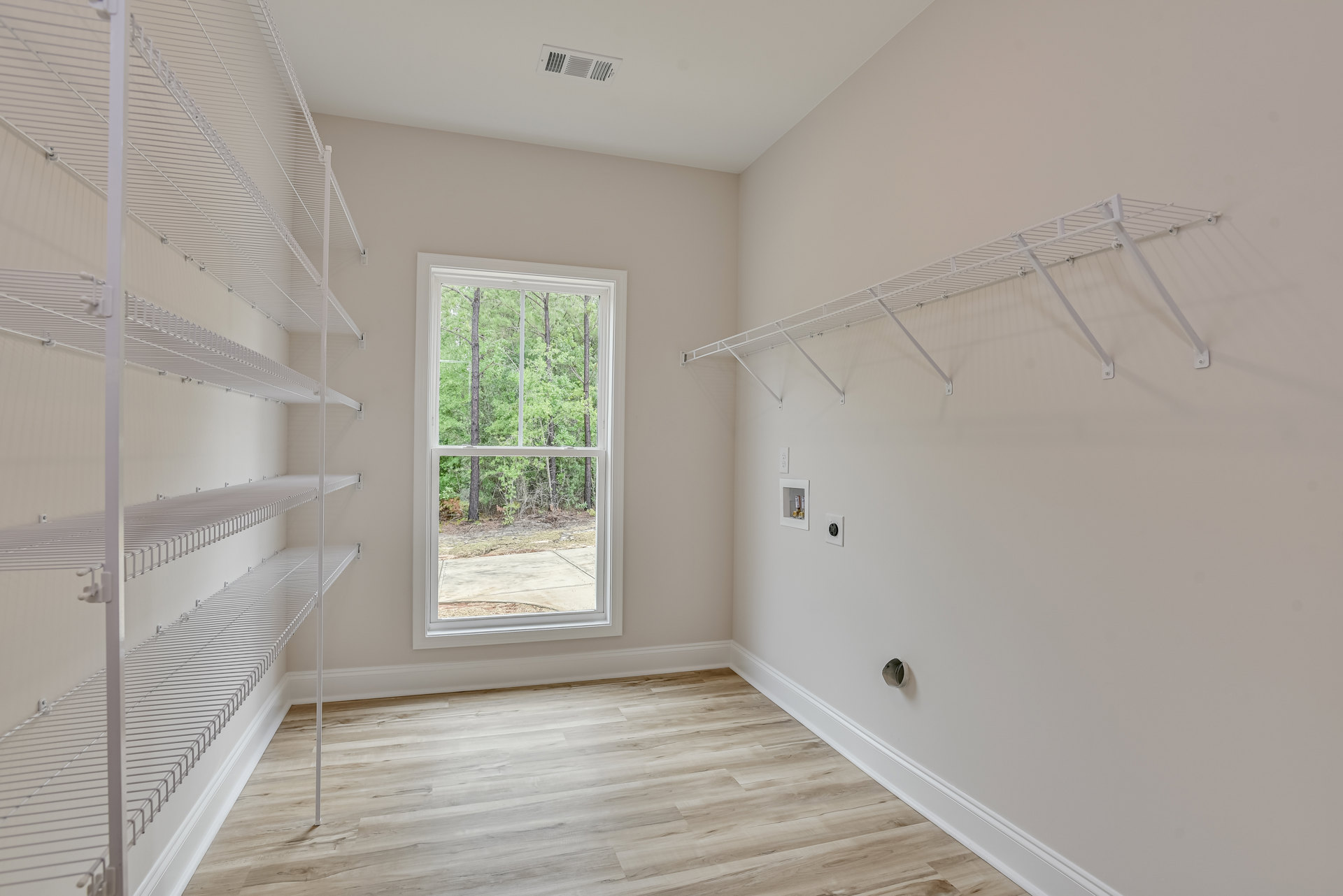 Empty closet with built-in white shelves, wood flooring, and a window overlooking trees.