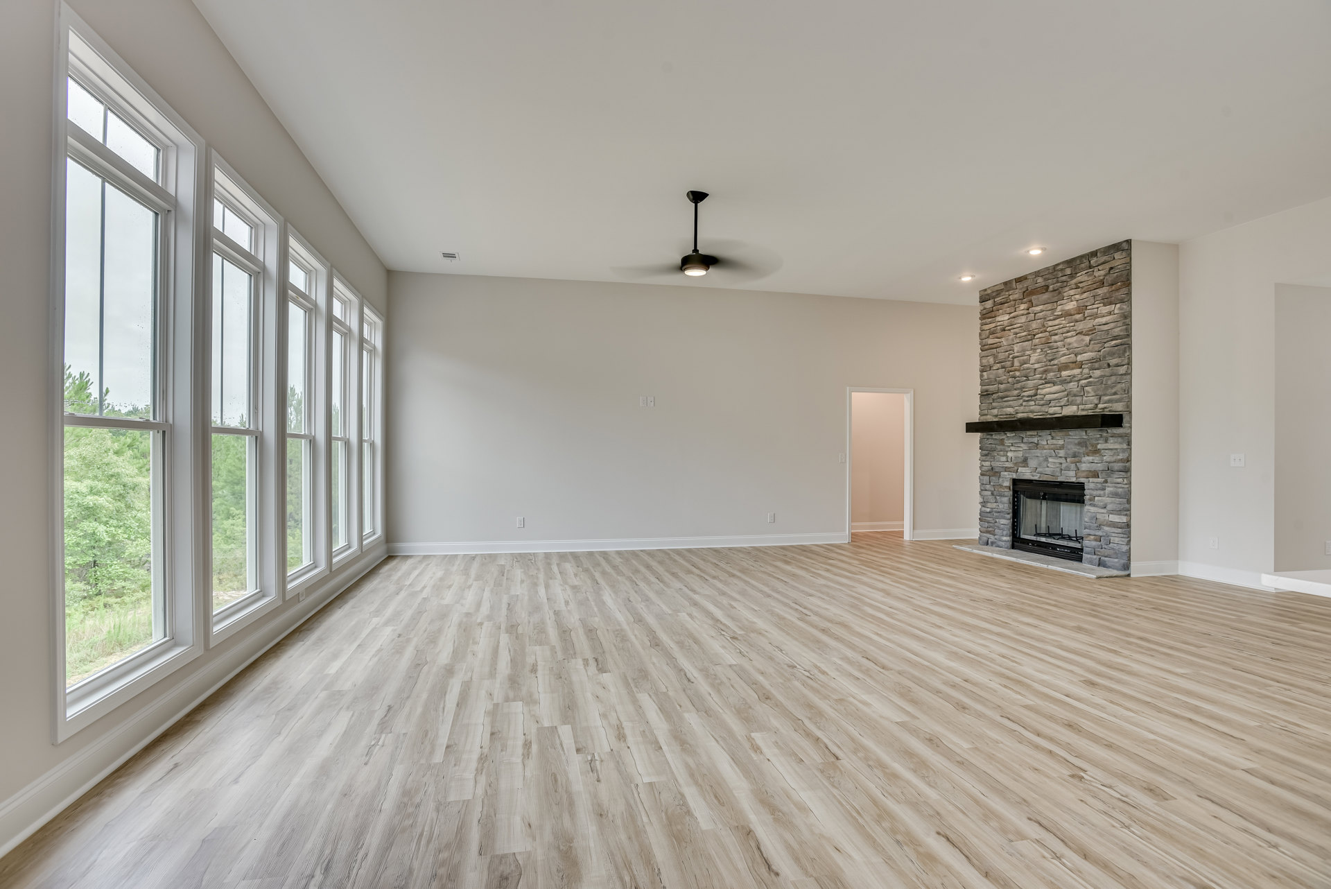 Spacious room with light wood flooring, white plaster walls, modern fireplace featuring a wood mantel and glass front, black support pole, and white door adjacent to a pink accent