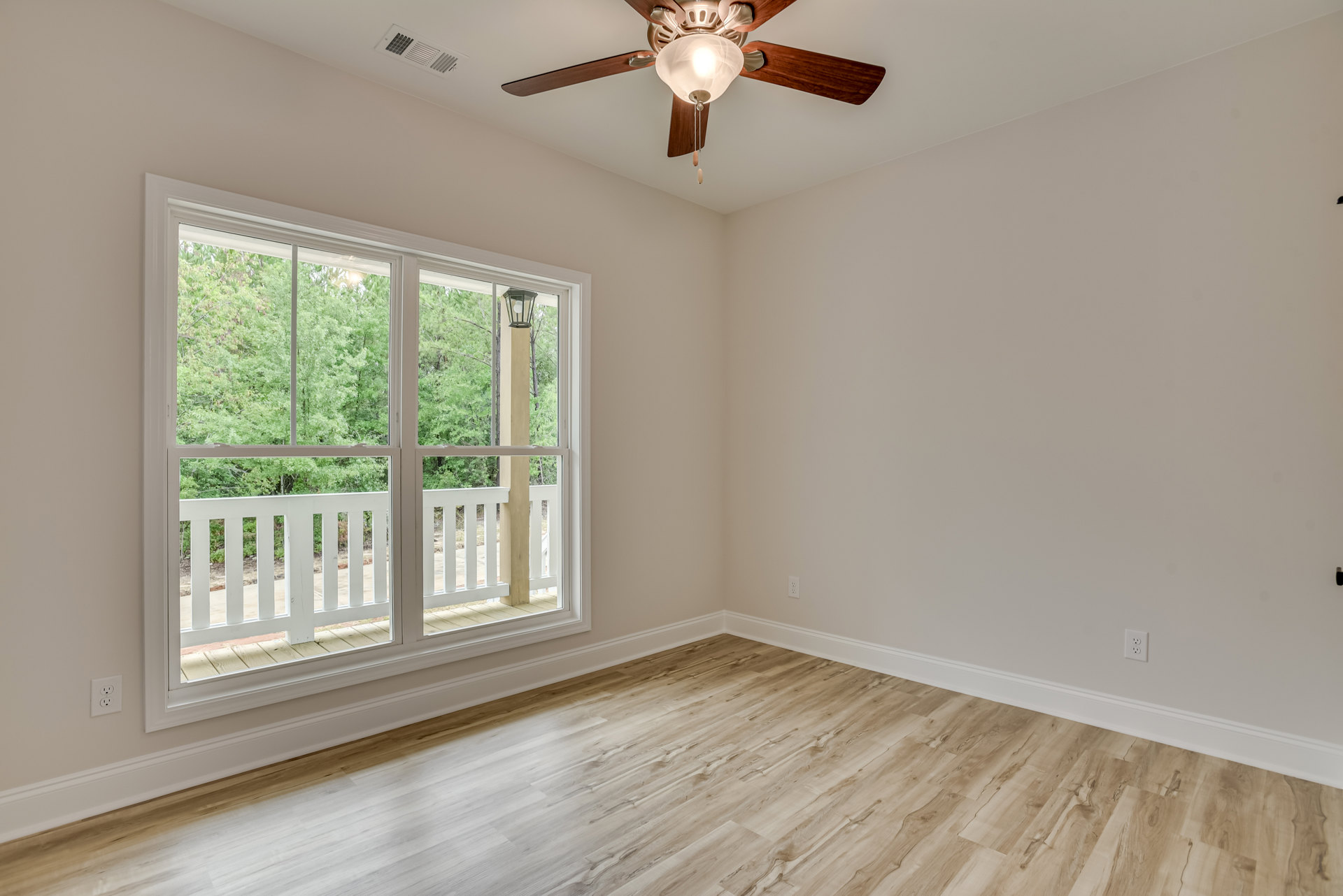 Ceiling fan with light fixture mounted on white plaster ceiling, large window overlooking porch and trees, wood flooring throughout room