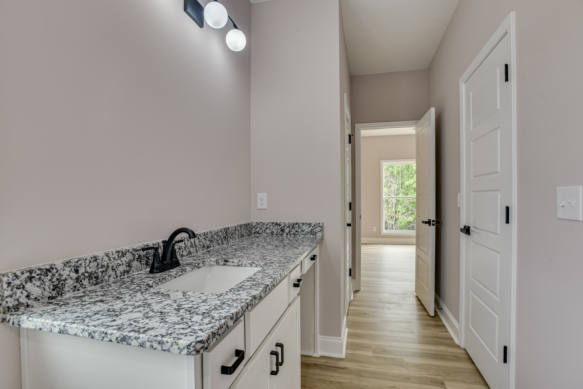 Bathroom with marble countertop, black faucet, wood floor, white cabinetry, window overlooking trees, and light switch on wall