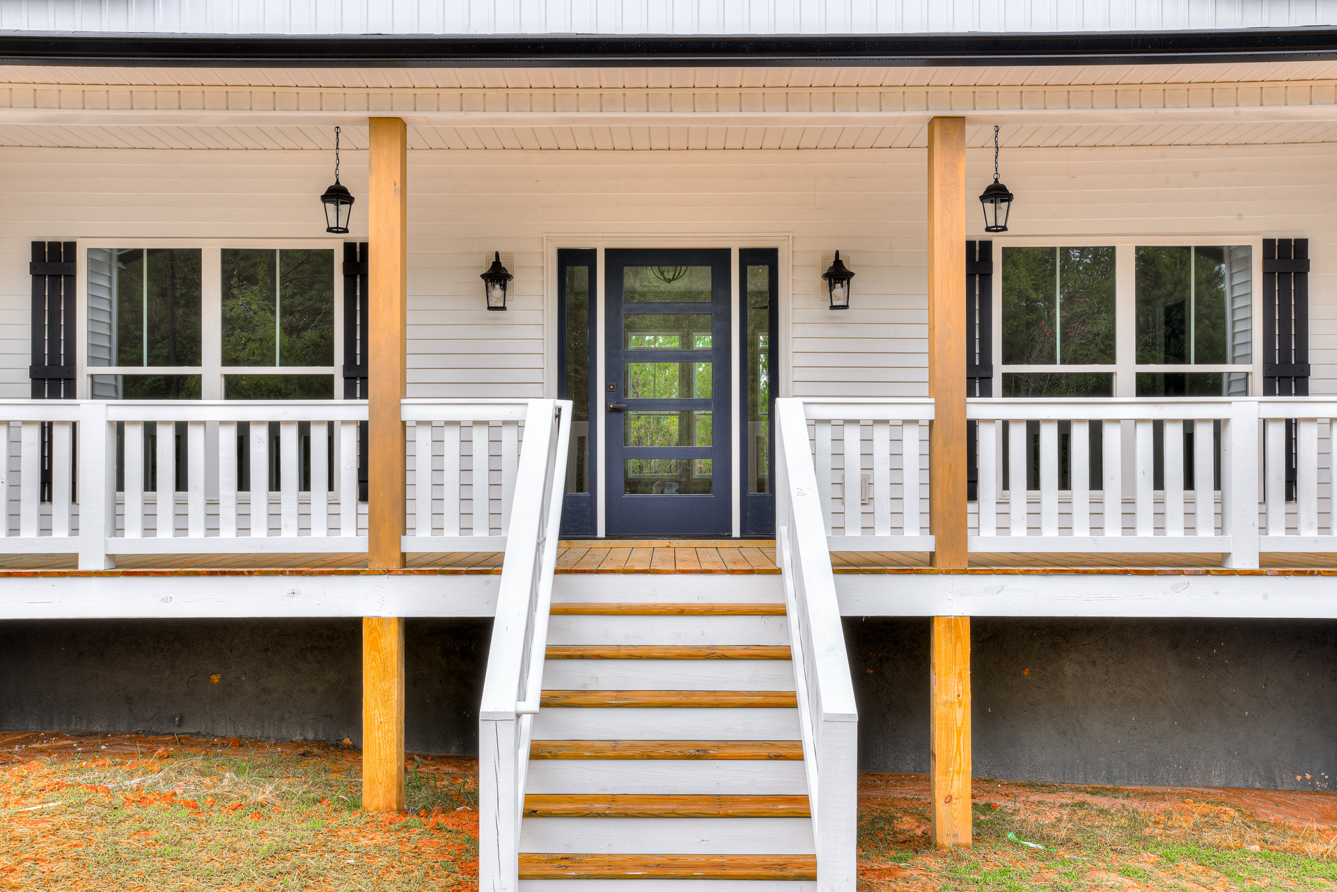 White siding exterior with blue door featuring glass panels, white stairs and deck with wooden railing, porch accented by balusters and handrail, potted plants near entry.