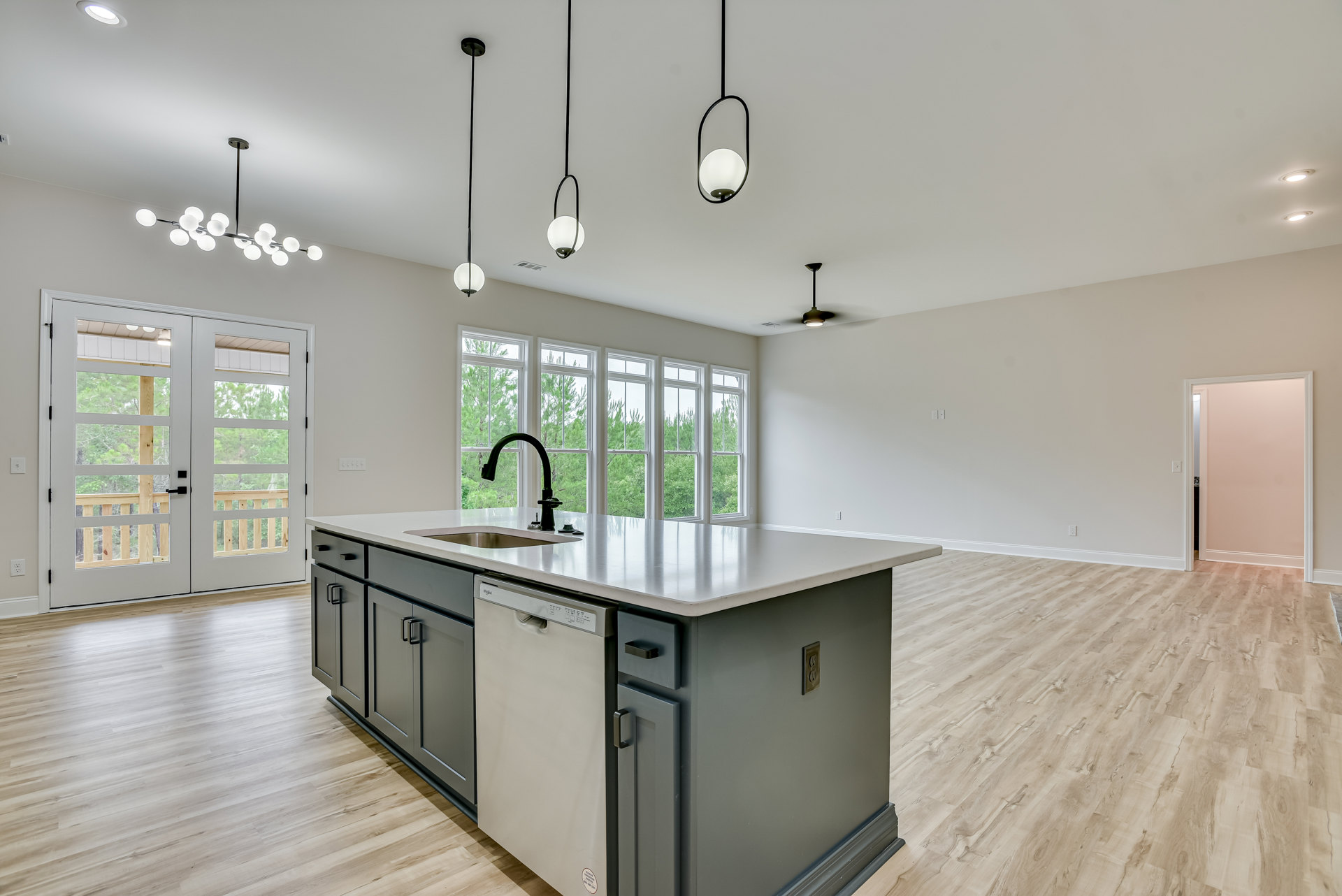 Modern kitchen featuring a black faucet and stainless steel sink set in a light countertop, built-in dishwasher, white cabinetry, glass-paneled double doors, and a close-up of a