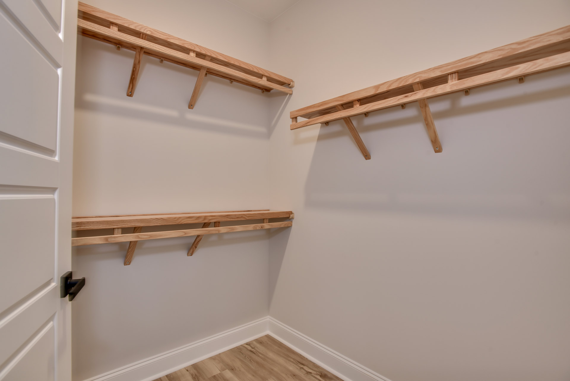 Closet with built-in wooden shelves, white door with black handle, hardwood plank flooring, plaster walls with crown molding