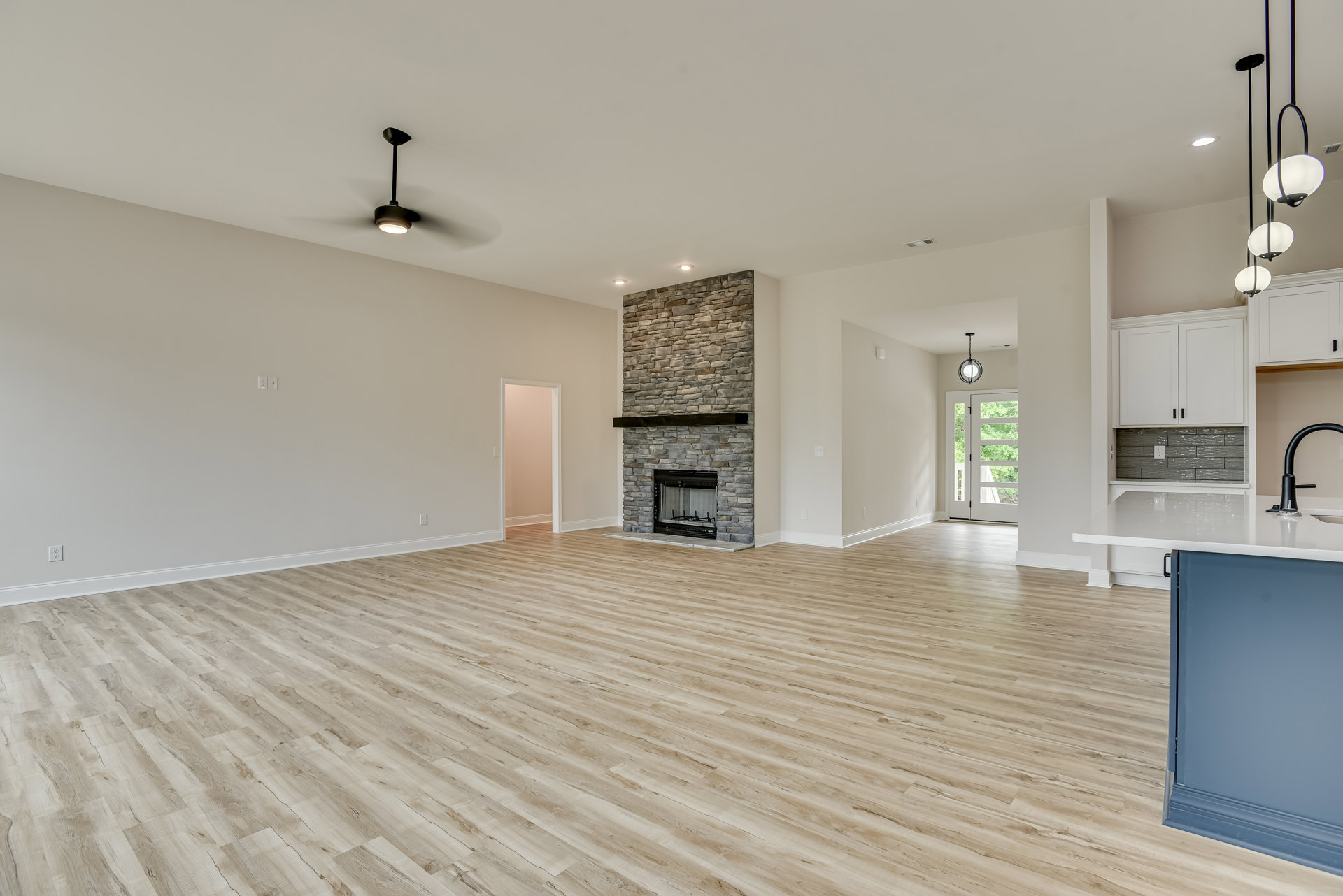 Spacious living area featuring hardwood flooring, central fireplace with glass front and wood mantel, blue accent wall, white ceiling, and built-in cabinetry