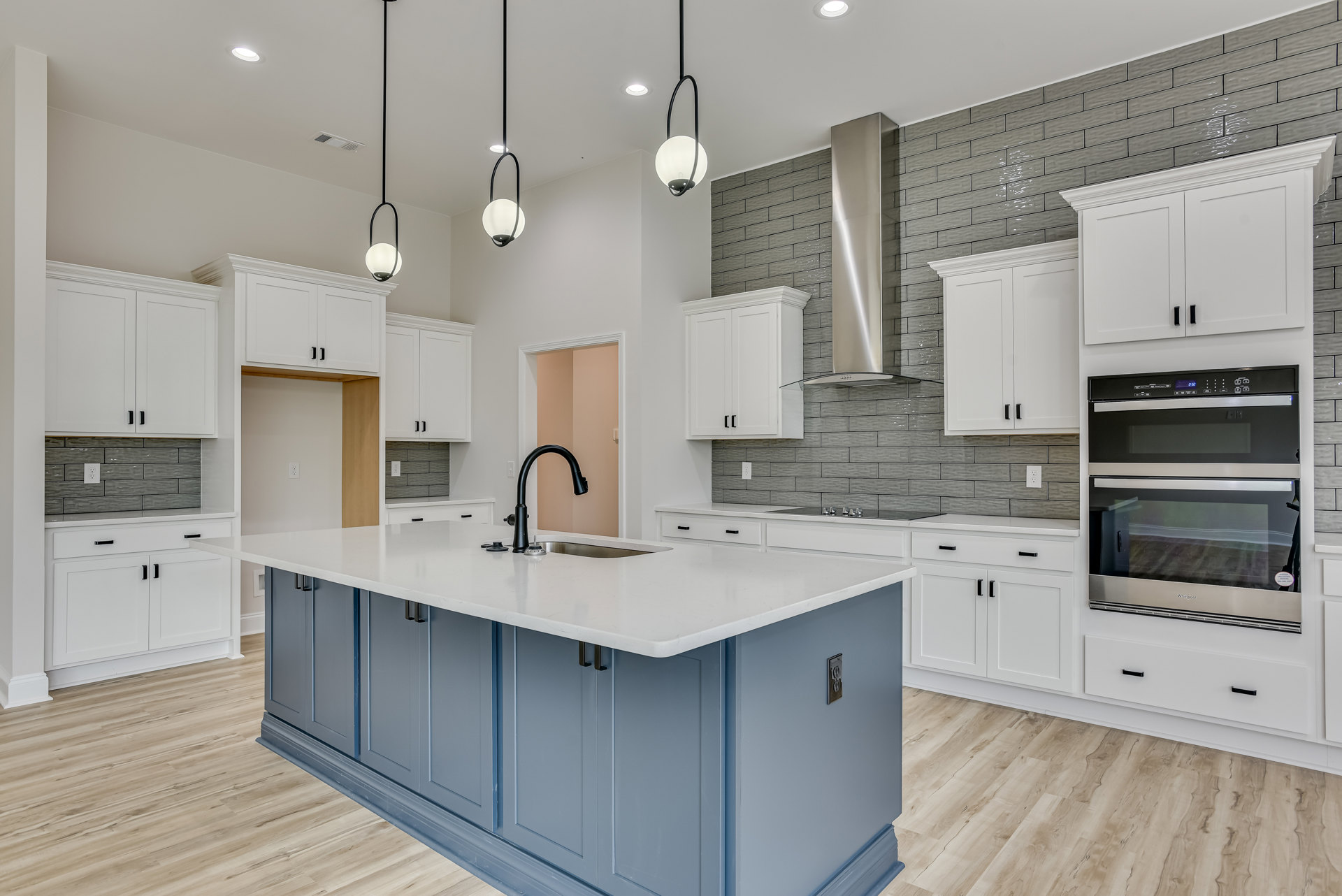 Spacious kitchen featuring a large white island with quartz countertop, stainless steel oven and microwave, shaker-style cabinetry, pendant light fixtures, and wide plank flooring