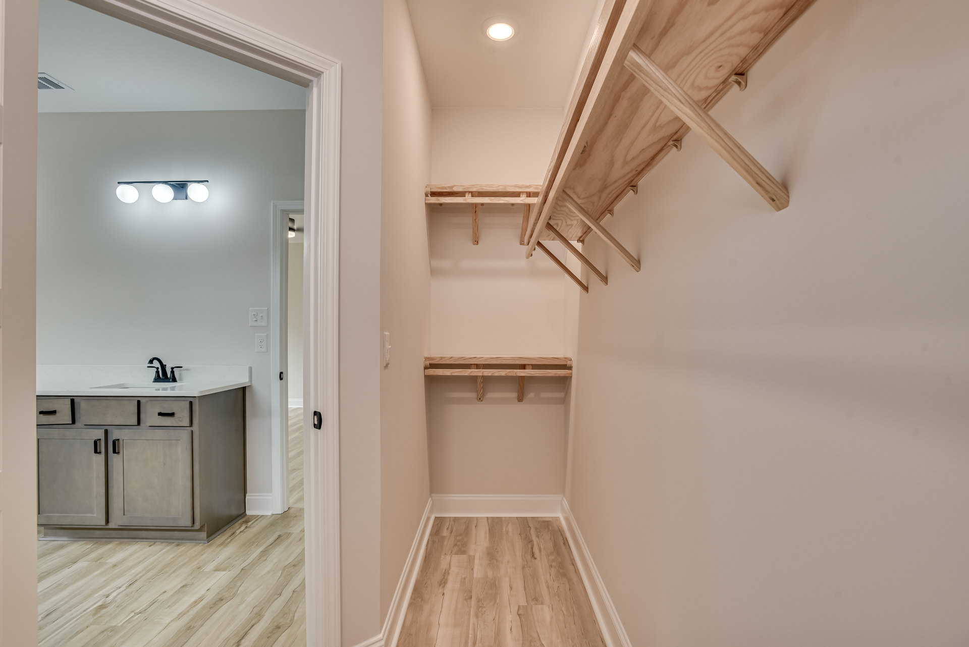 Hallway with built-in wood shelves, wood flooring with white trim, white plaster walls, recessed lighting, and a wooden table near a wall-mounted sink with chrome faucet