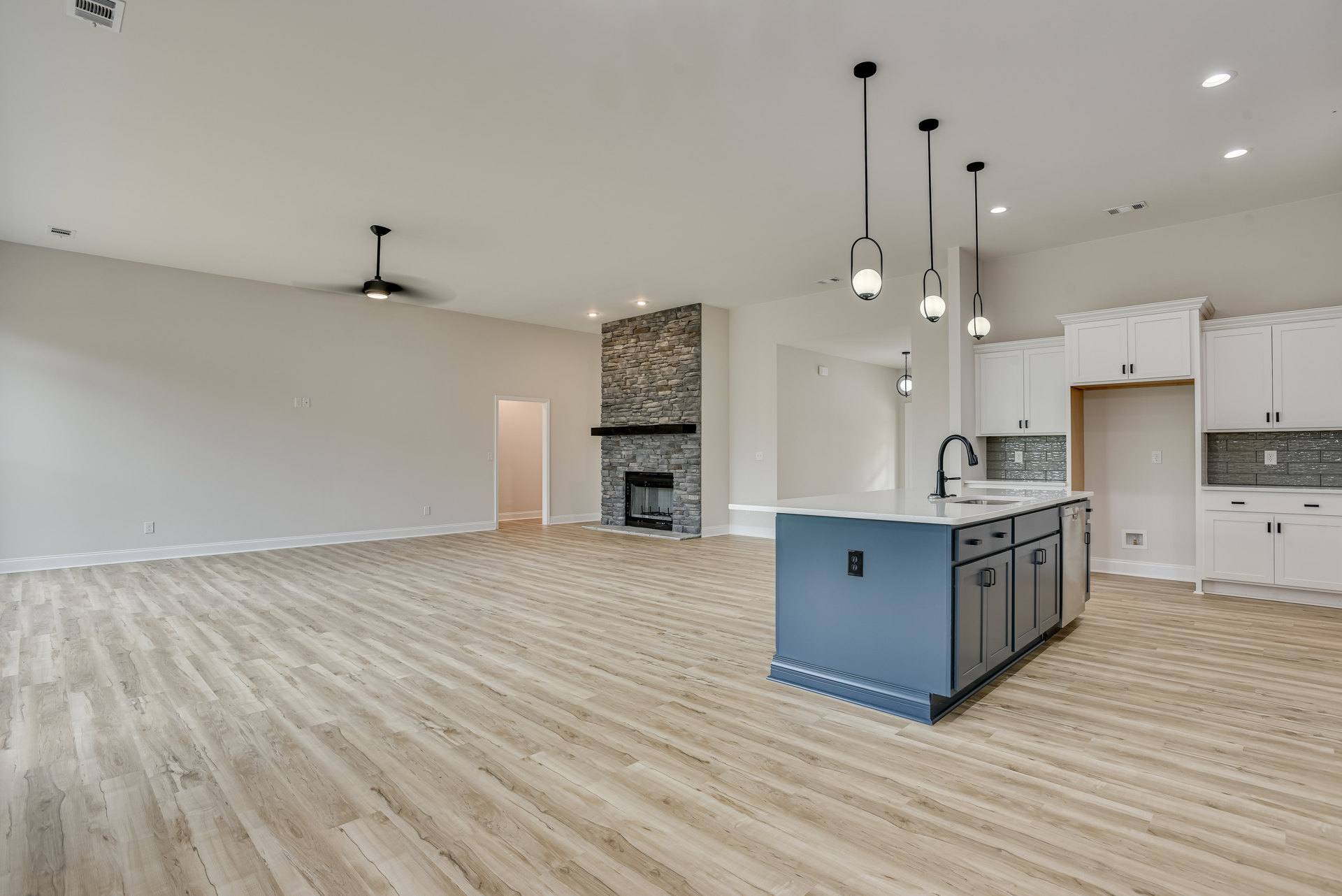 Spacious kitchen and living area featuring a hardwood floor, blue kitchen island with sink and black faucet, white walls, fireplace with black mantel, and adjacent door with light