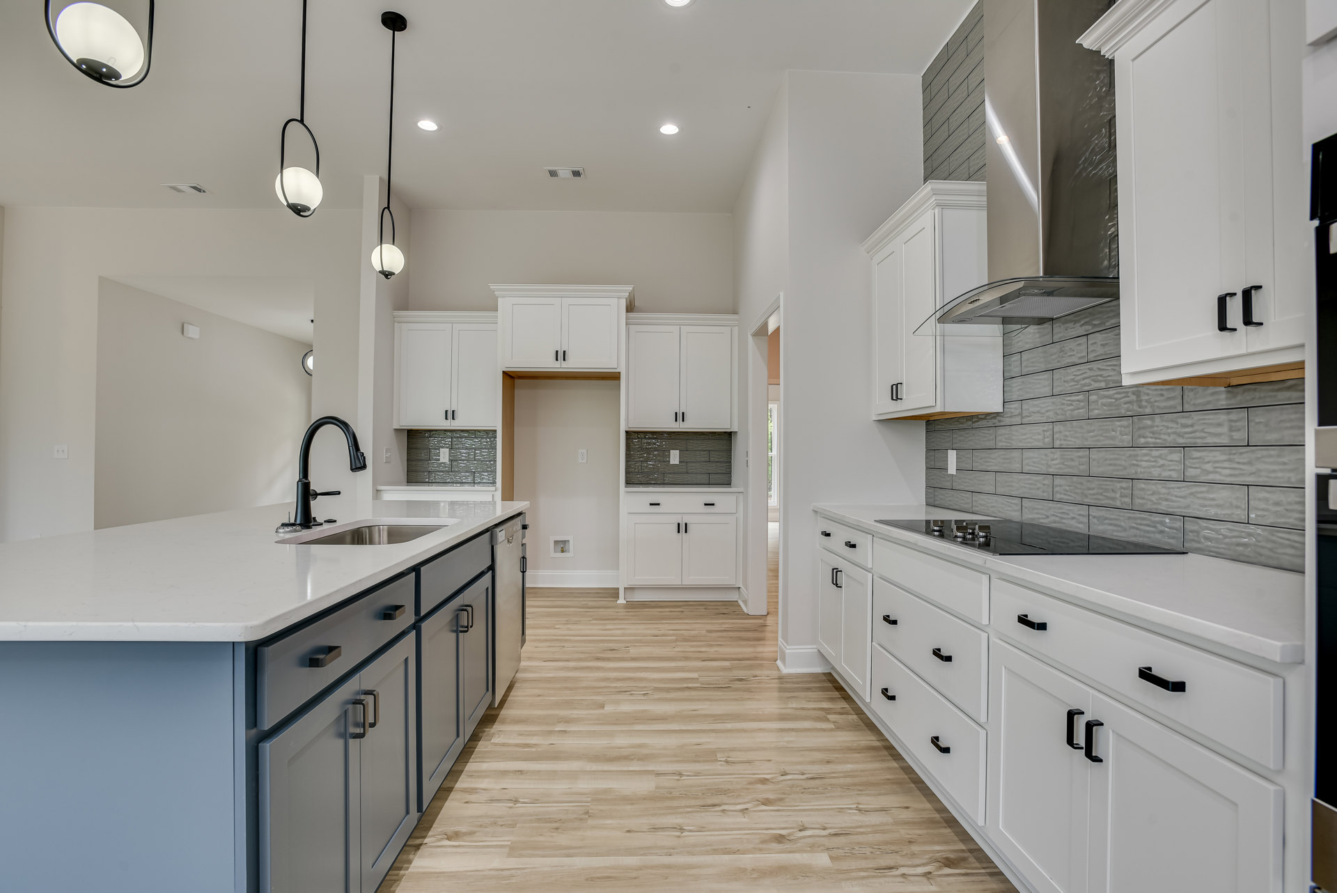 Kitchen with white shaker cabinets, wood plank flooring, central island featuring a black faucet and undermount sink, quartz countertops, and modern pendant lighting