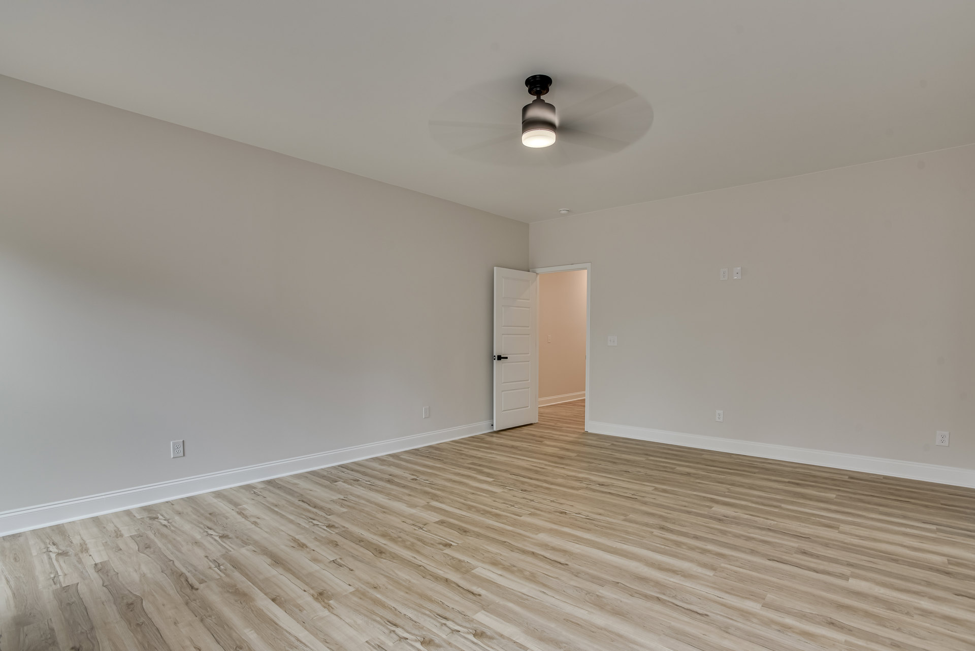 Room with wood flooring, white door with black handle, ceiling fan, light fixture, and light switch on plaster wall